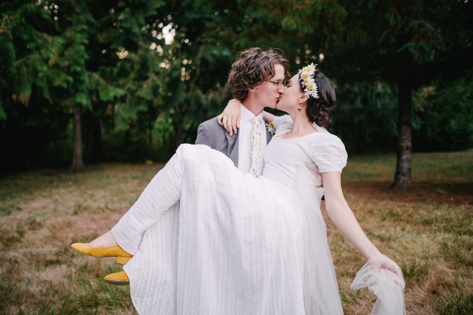  Groom carries bride in front of trees while kissing 