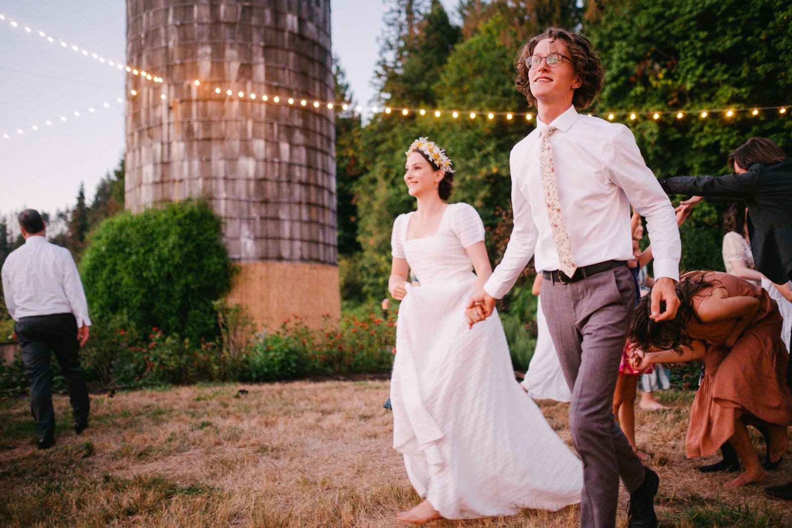  Bride and groom holding hands running through English line with twinkle lights behind them 