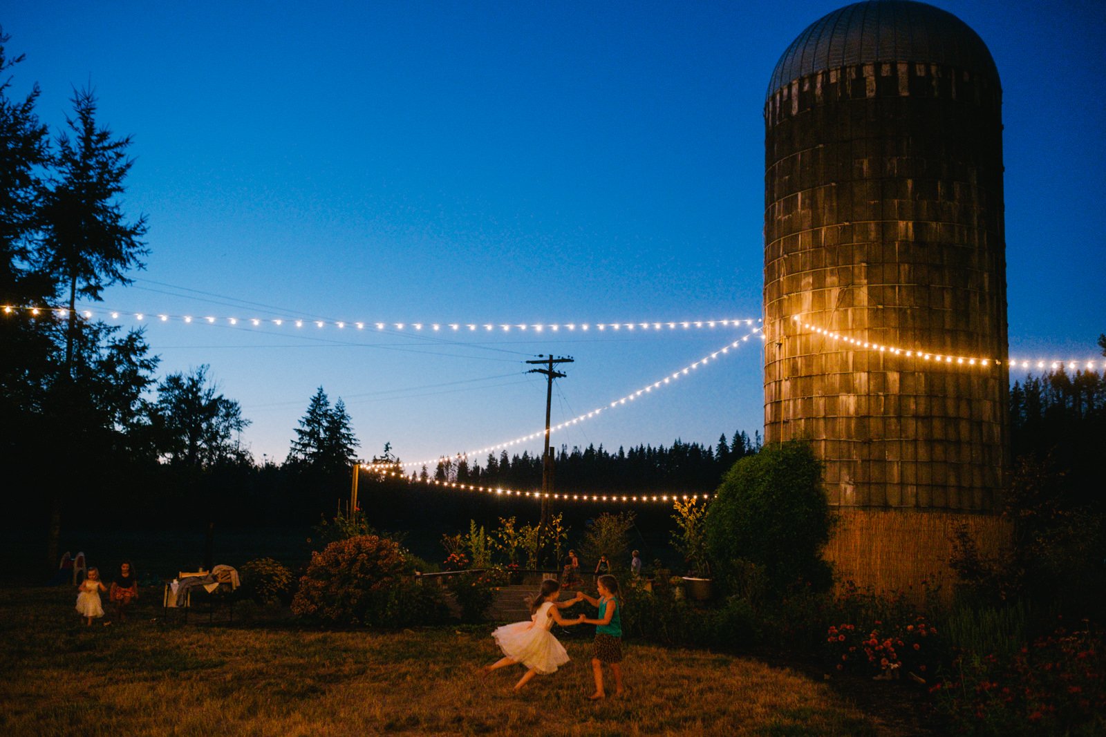  Kids twirl each other at blue hour under twinkle lights at Clackamas River Farm 