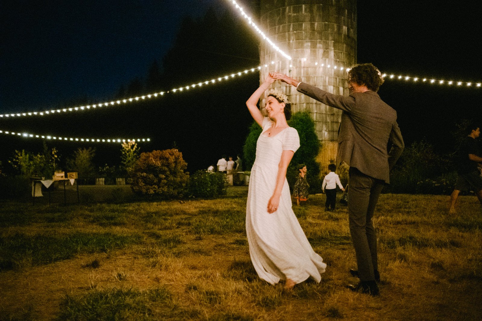  Bride spins with groom under twinkle lights and silo 