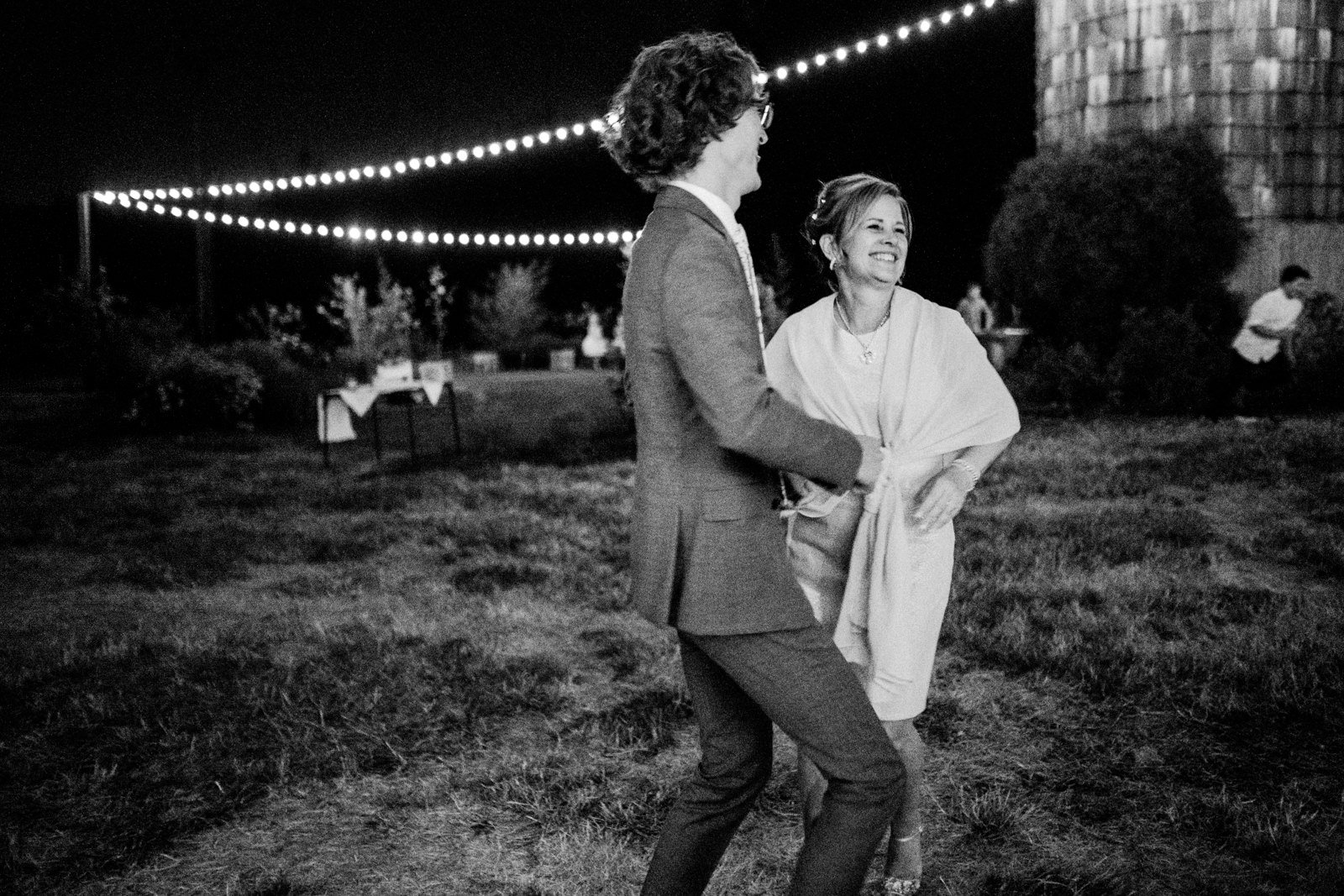  Groom dances with mother under twinkle lights in field 