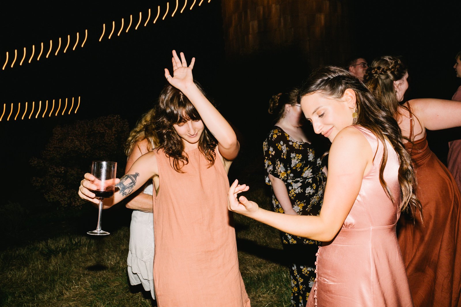  Bridesmaids dance together with wine glass in twinkle lights 