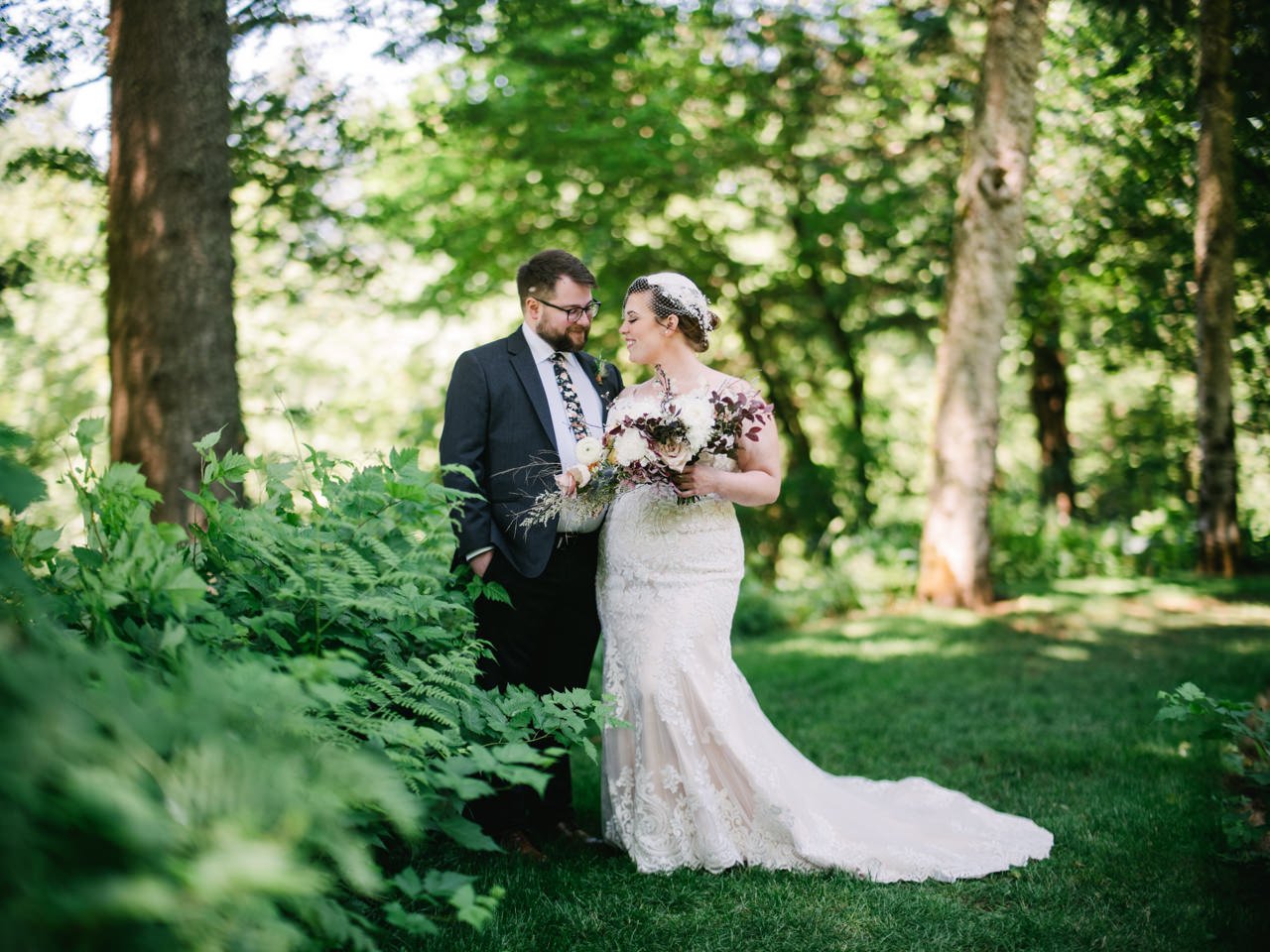  Bride and groom smile together in grassy path surrounded by ferns 