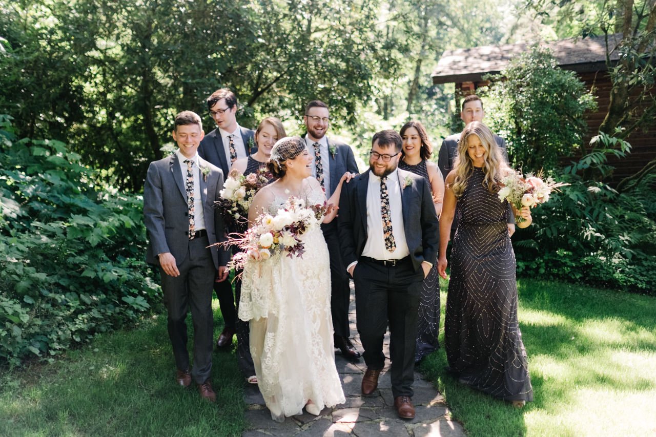  Wedding party walks together in sunlight laughing in floral ties and blue dark dresses 
