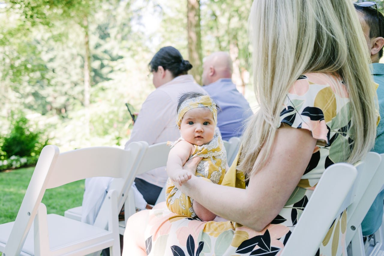  Baby in yellow floral jumper sits on lap waiting for ceremony 