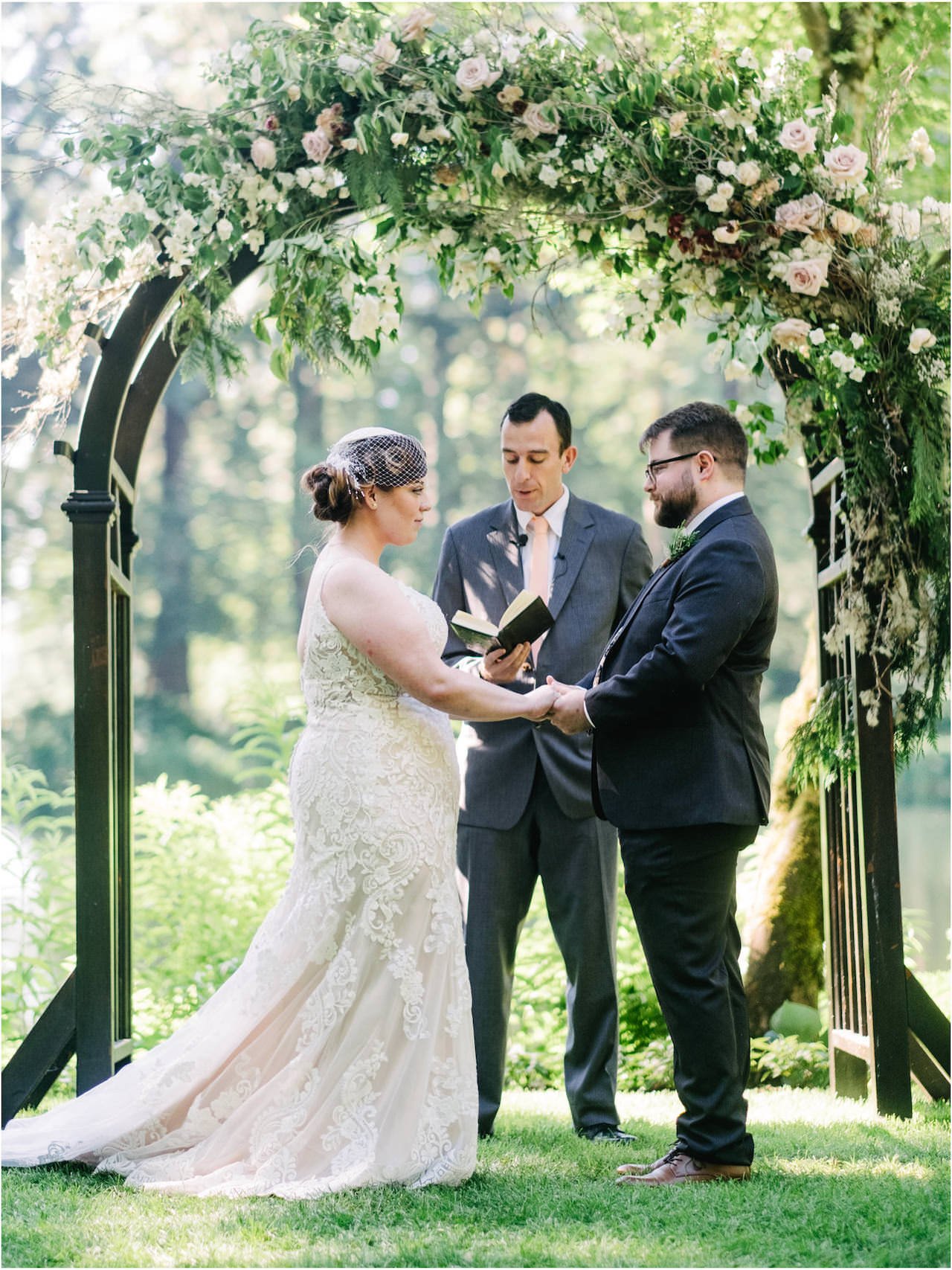  Vertical photo of bride and groom holding hands under rose floral arch 