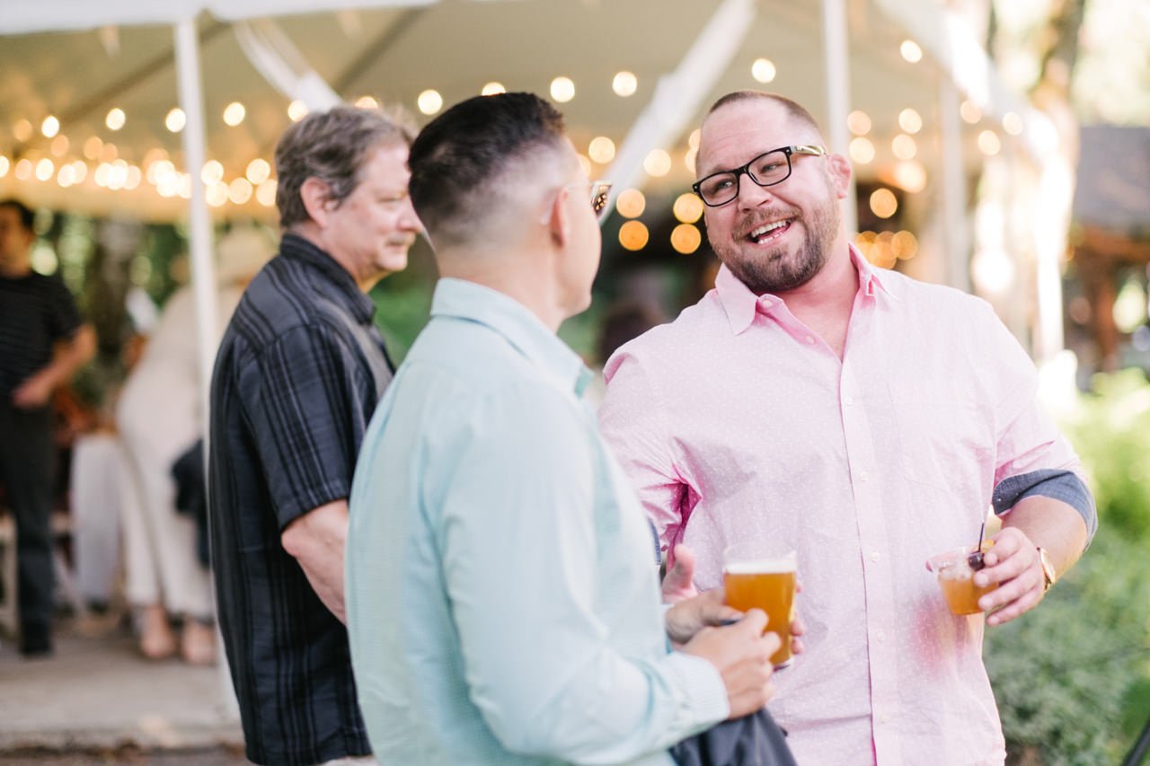  Wedding guest in pink collared shirt share laugh over beer and drinks 