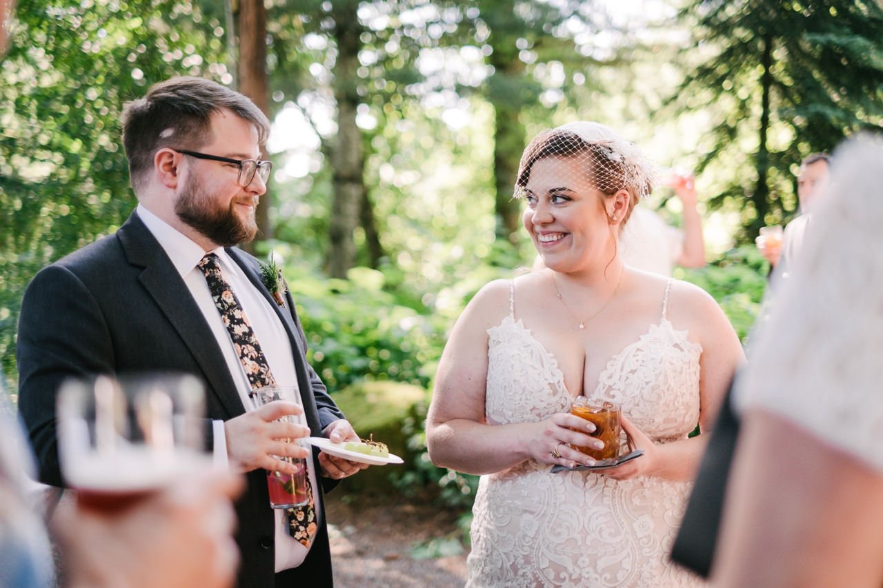 Bride gives knowing smile to groom while they hold specialty drinks during cocktail hour 