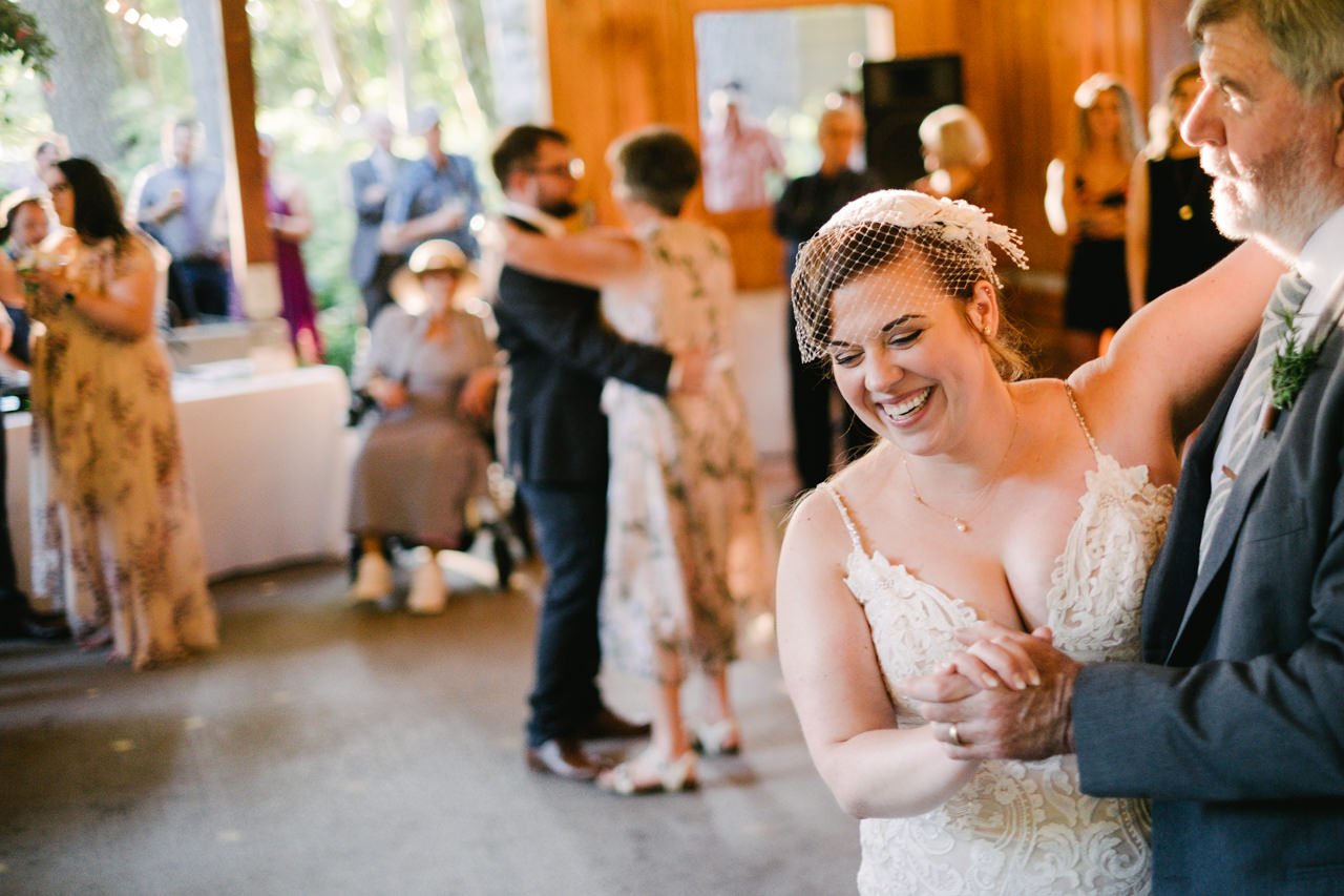  Bride laughs while dancing with dad in warm sunlight 