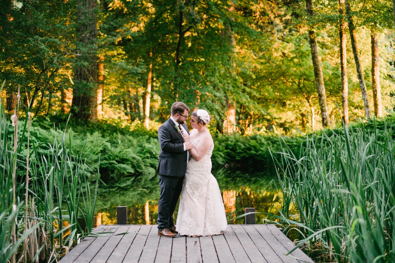  Married couple stands on dock surrounded by ferns and cattails 