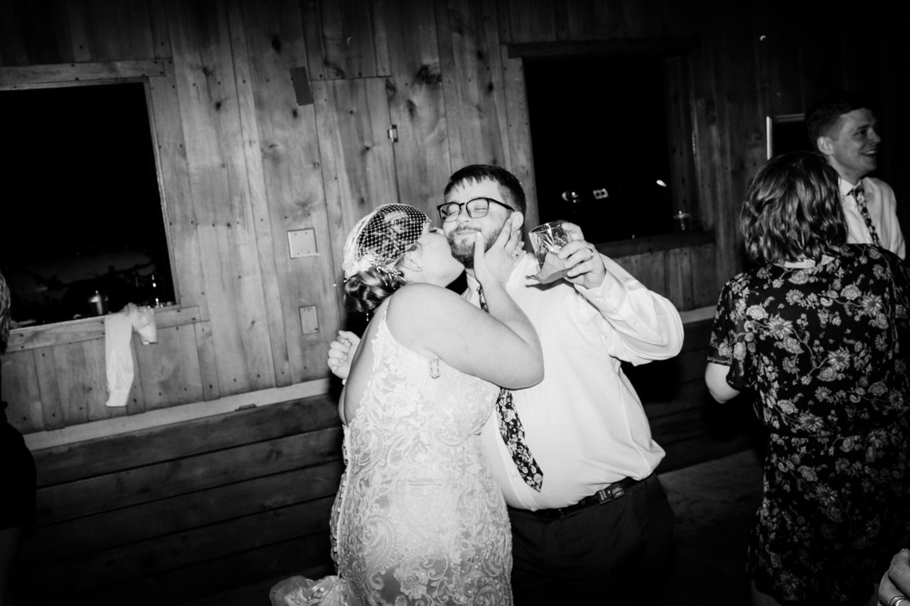  Bride kisses groom holding drink at end of night 