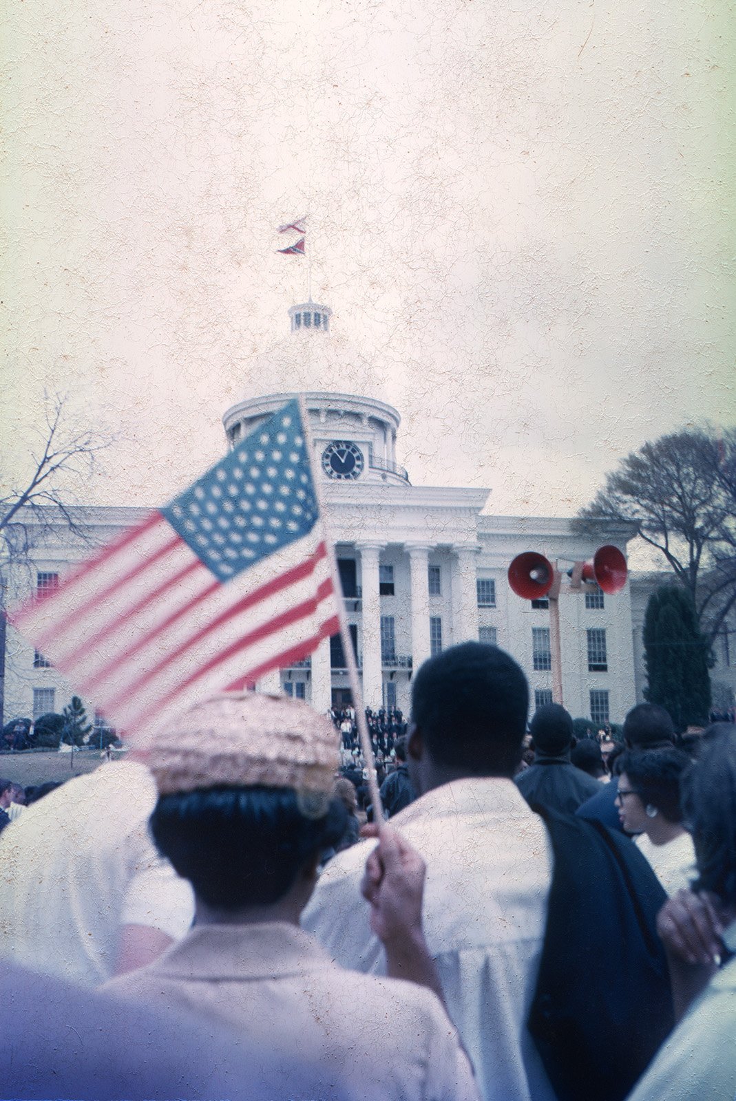 At the Alabama State Capitol. Note the flags flying atop the capitol, Alabama state flag on top, confederate flag below. The only US flag in this photo is being held by a marcher.
