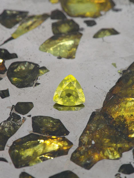 This picture shows a 1.12 carat peridot taken from the Esquel meteorite sat on a polished slice of it