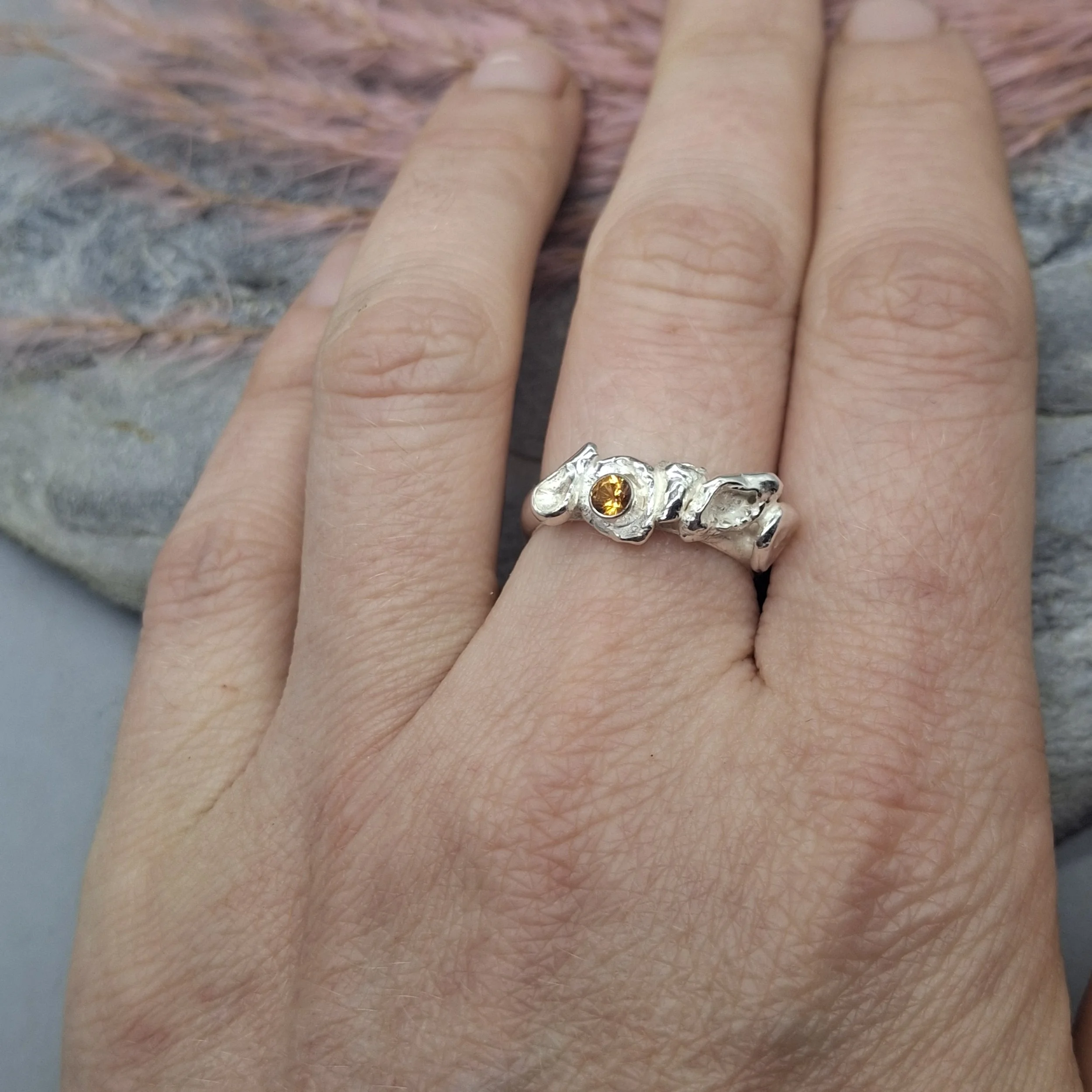 Handmade sterling silver Fallen Blossom ring with organic water-cast silver petals, featuring a glowing mandarin garnet in warm orange tones, shown worn on the hand