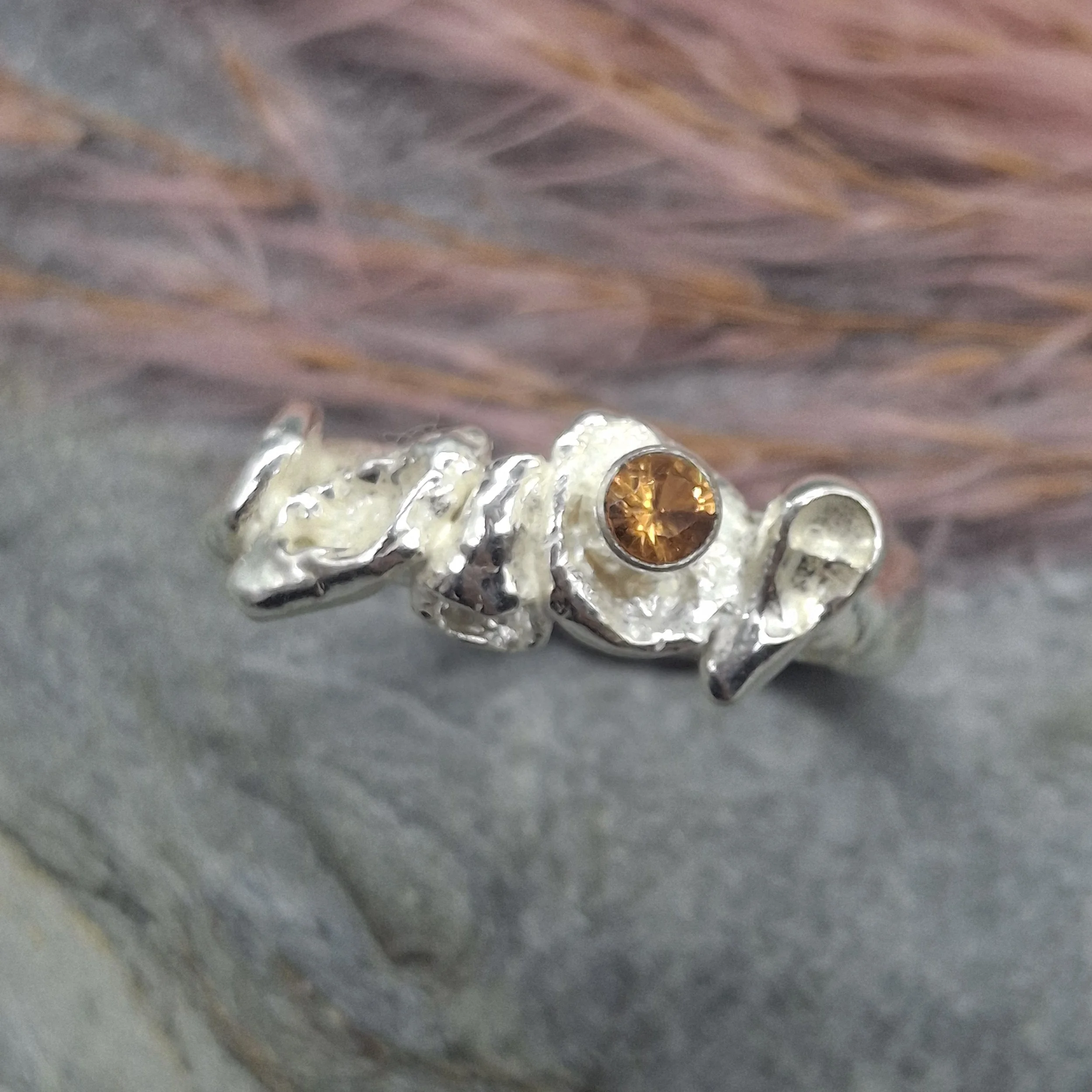 Handmade sterling silver Fallen Blossom ring with organic water-cast silver petals, featuring a glowing mandarin garnet in warm orange tones.