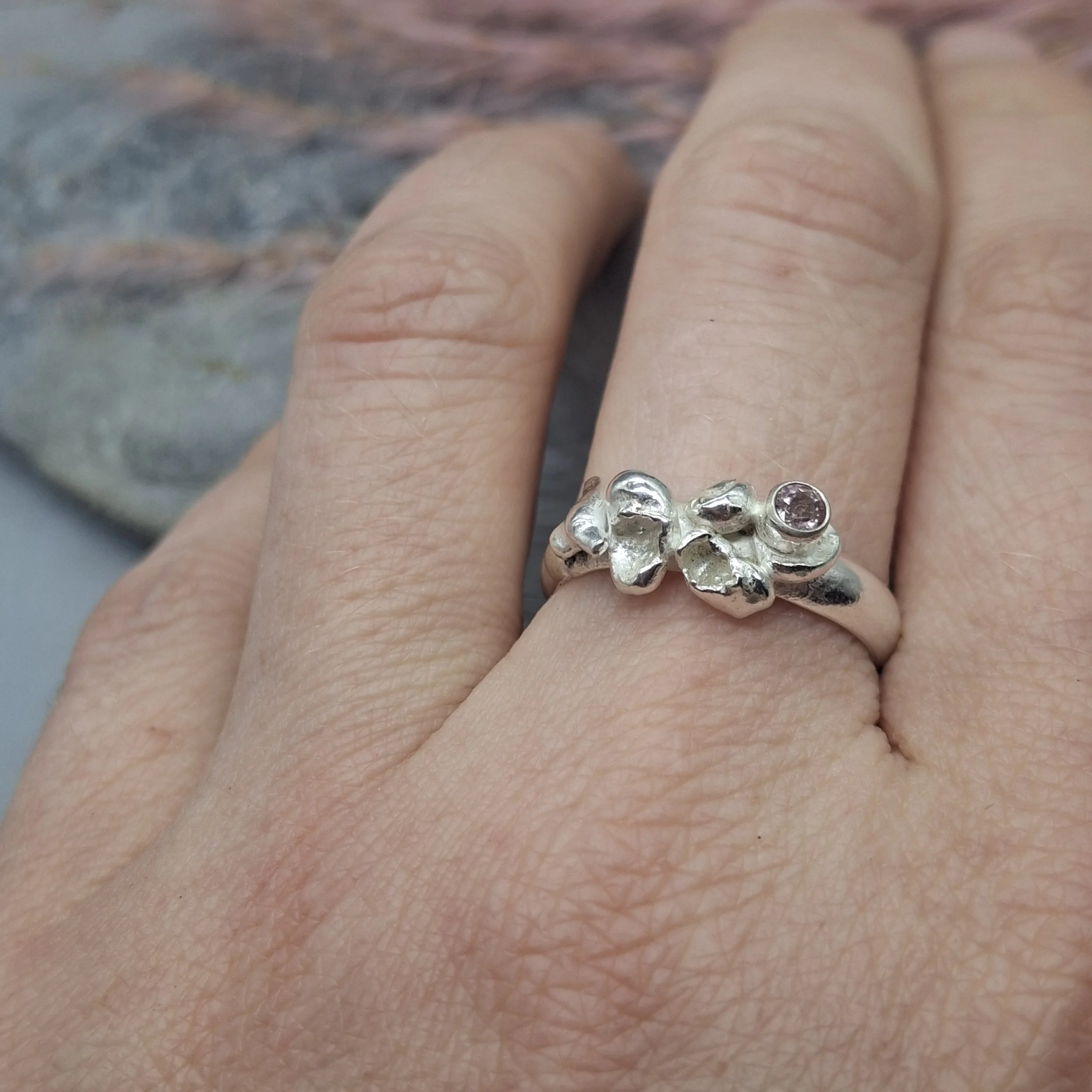 Handmade sterling silver Fallen Blossom ring with water-cast petal textures, featuring a pale pink tourmaline nestled in organic silver, shown worn on the hand