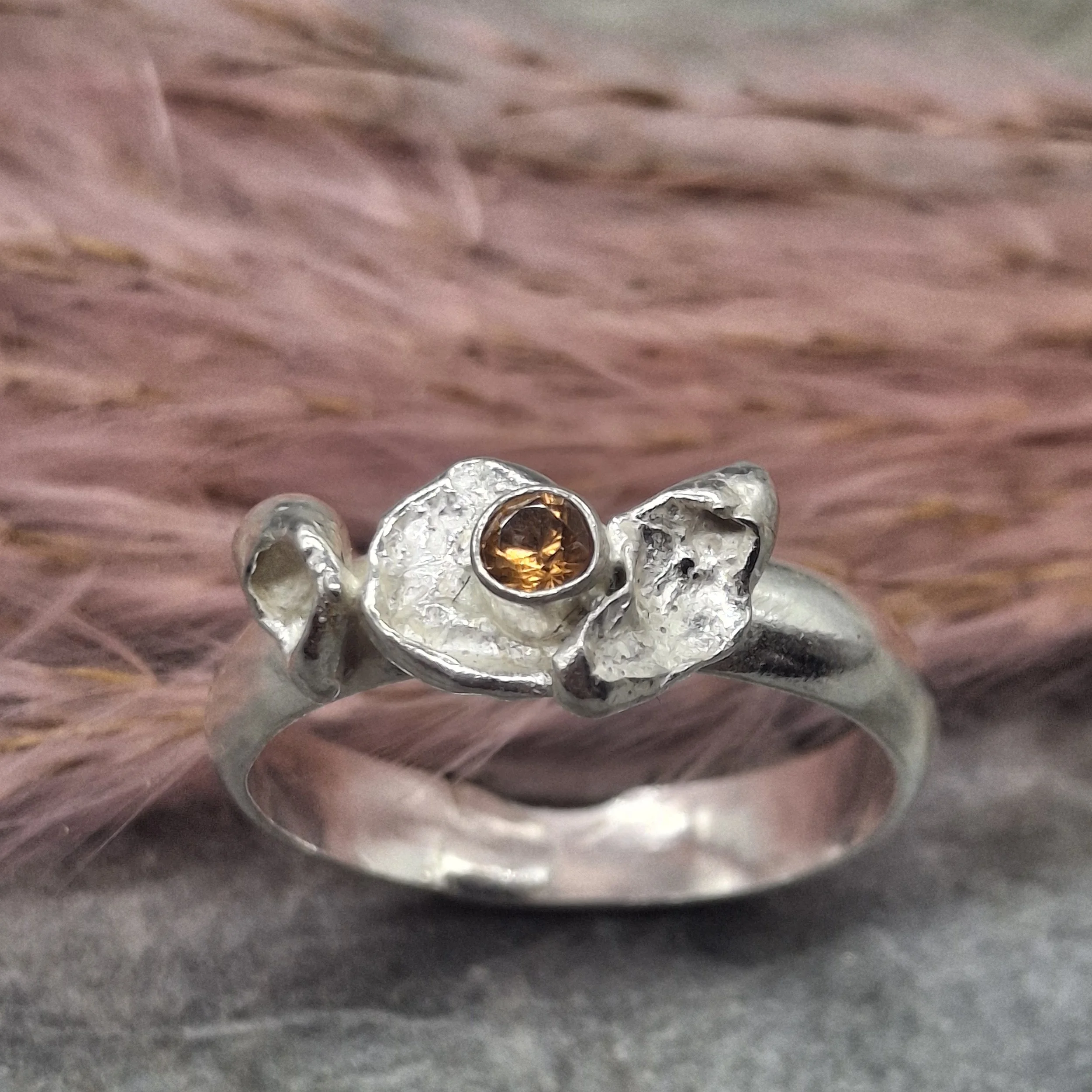 Handmade sterling silver Fallen Blossom ring with organic water-cast silver petals, featuring a glowing mandarin garnet in warm orange tones.