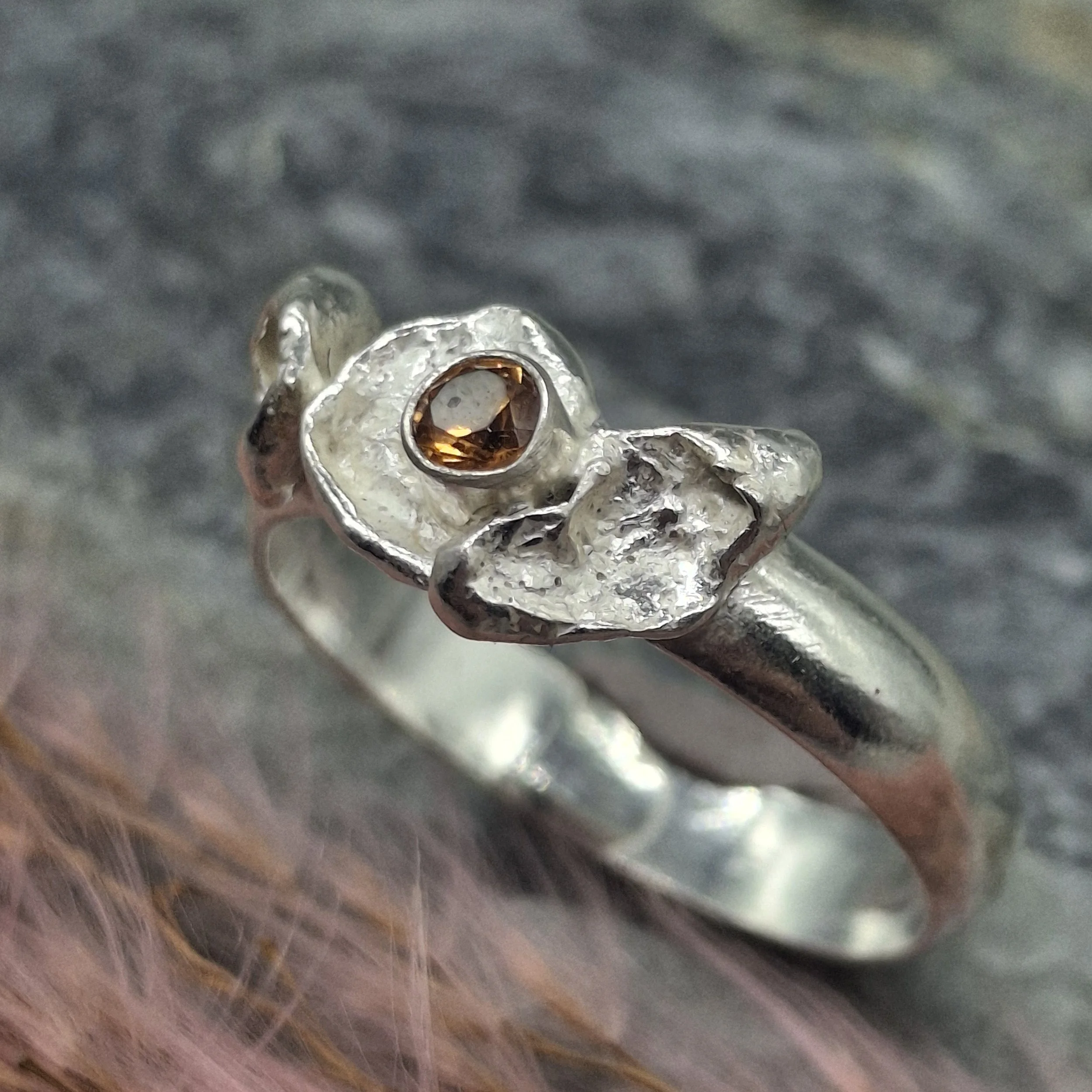Handmade sterling silver Fallen Blossom ring with organic water-cast silver petals, featuring a glowing mandarin garnet in warm orange tones.