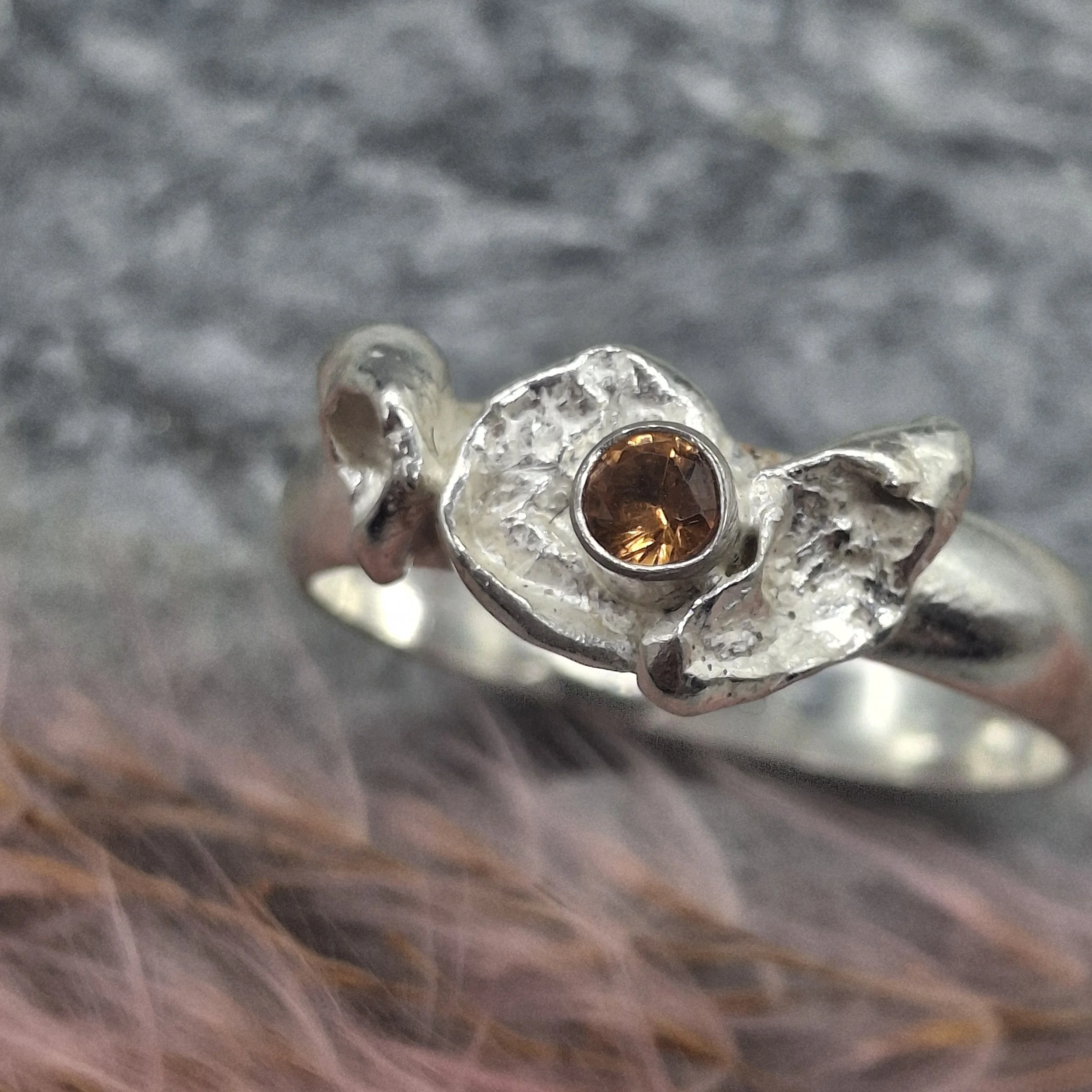 Handmade sterling silver Fallen Blossom ring with organic water-cast silver petals, featuring a glowing mandarin garnet in warm orange tones.