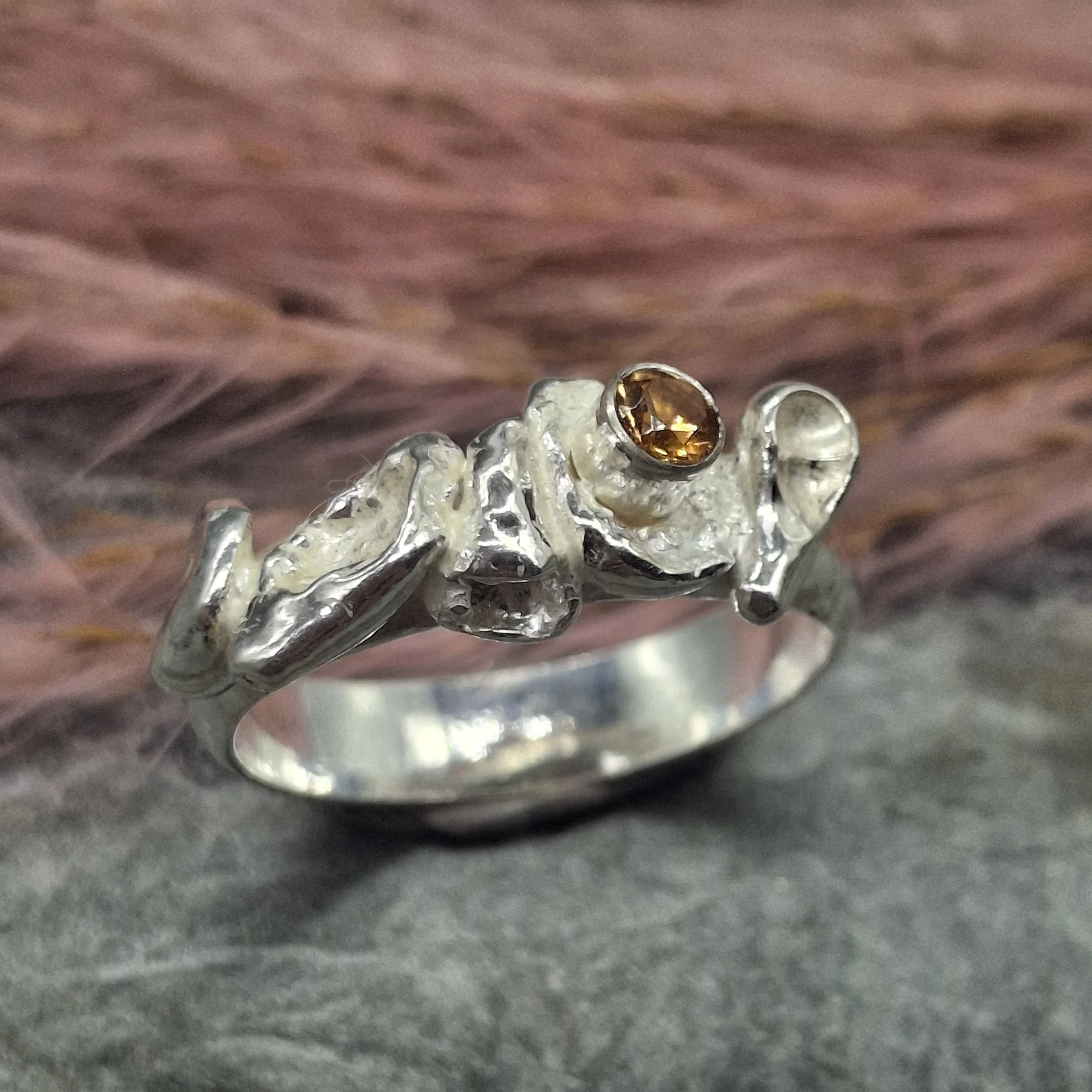 Handmade sterling silver Fallen Blossom ring with organic water-cast silver petals, featuring a glowing mandarin garnet in warm orange tones.