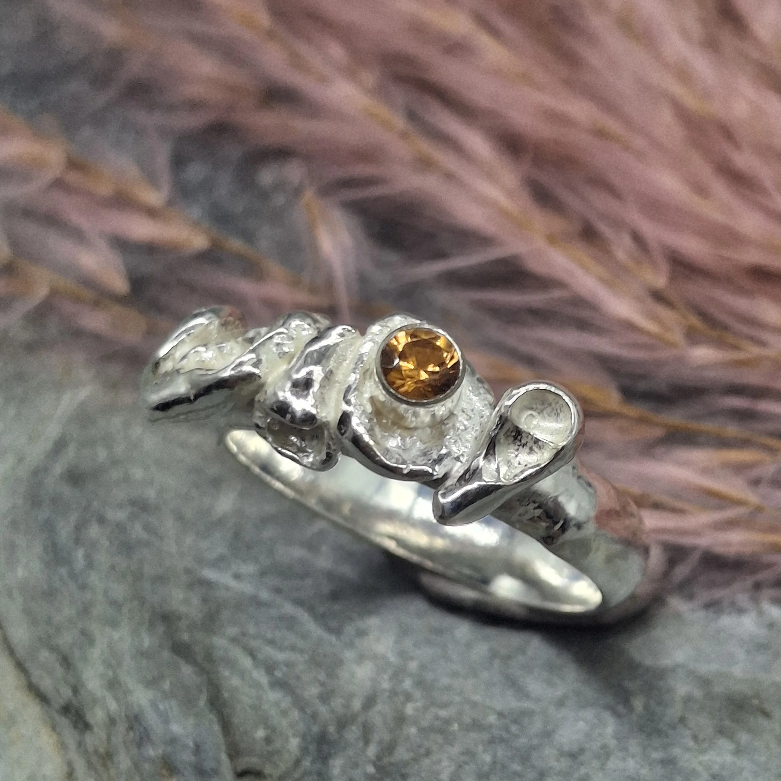 Handmade sterling silver Fallen Blossom ring with organic water-cast silver petals, featuring a glowing mandarin garnet in warm orange tones.