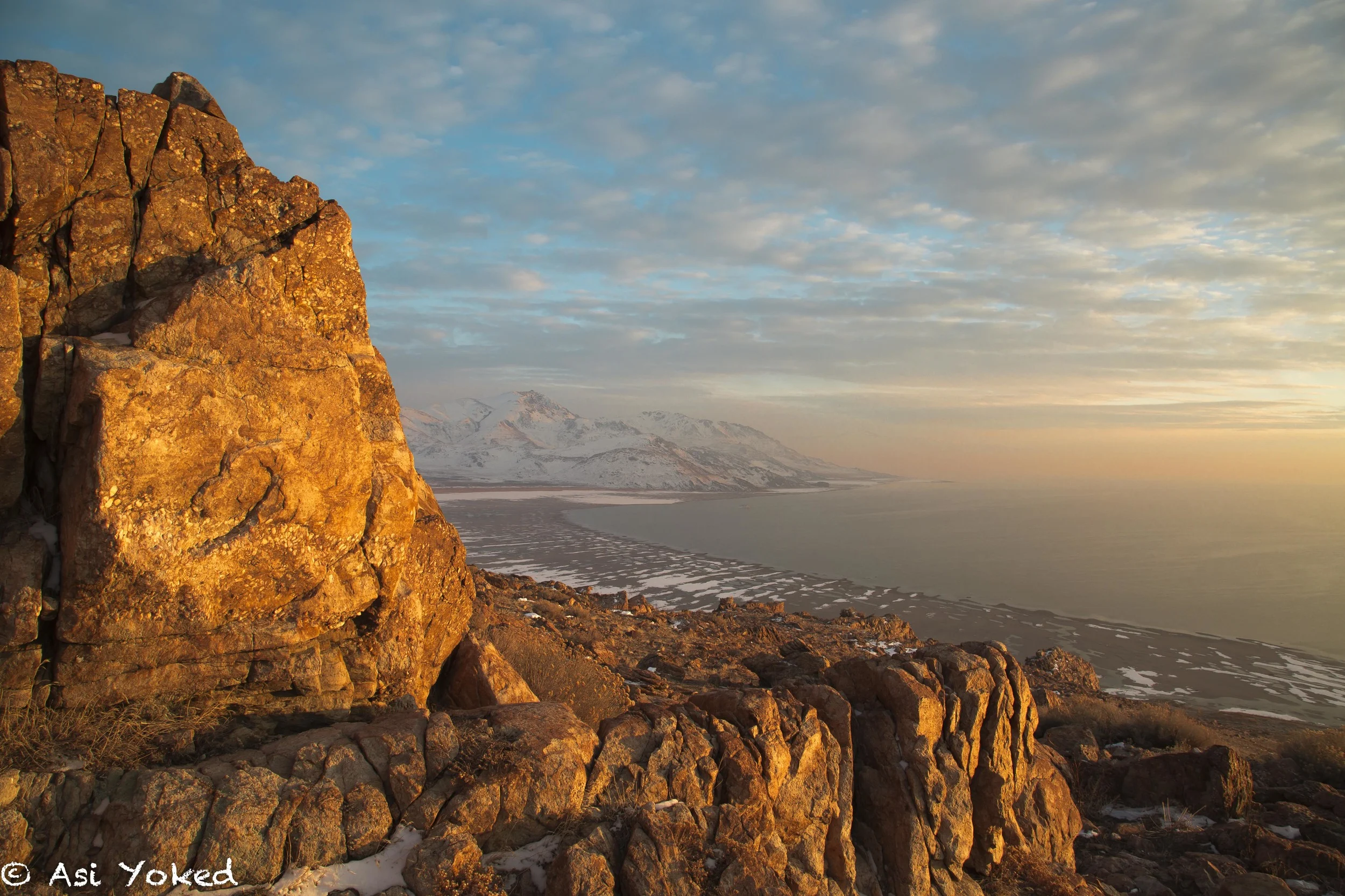 Sunlit rocky cliff with mountain ranges and oceanview in the background during sunset or sunrise.