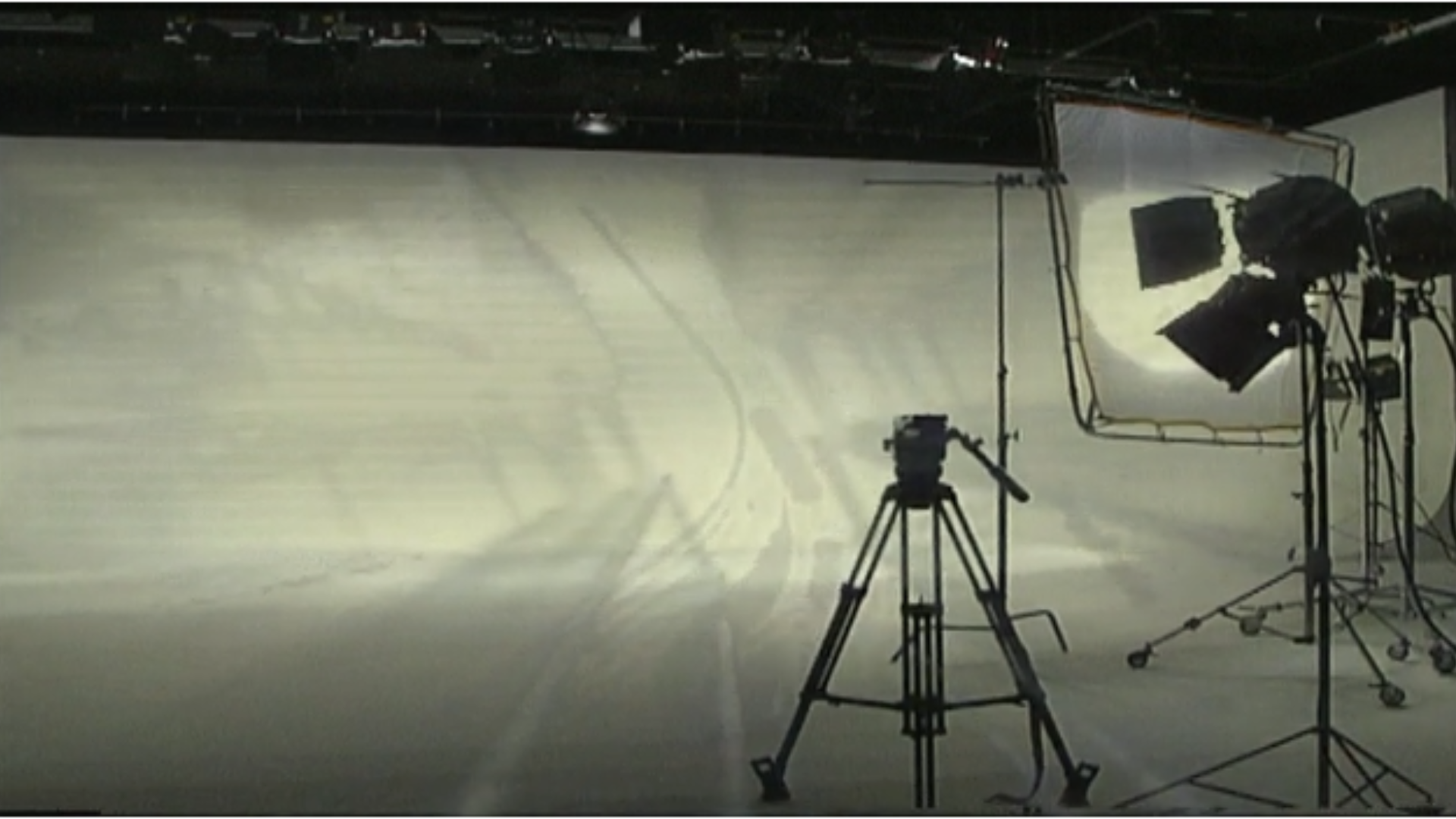 Photography equipment including a camera on a tripod and studio lights set up in front of a large white curtain or backdrop.