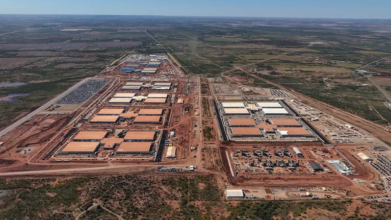 Aerial view of a large data-center campus under construction in a rural landscape, with multiple rectangular buildings, service roads, construction areas, utility infrastructure, and open land extending to the horizon.