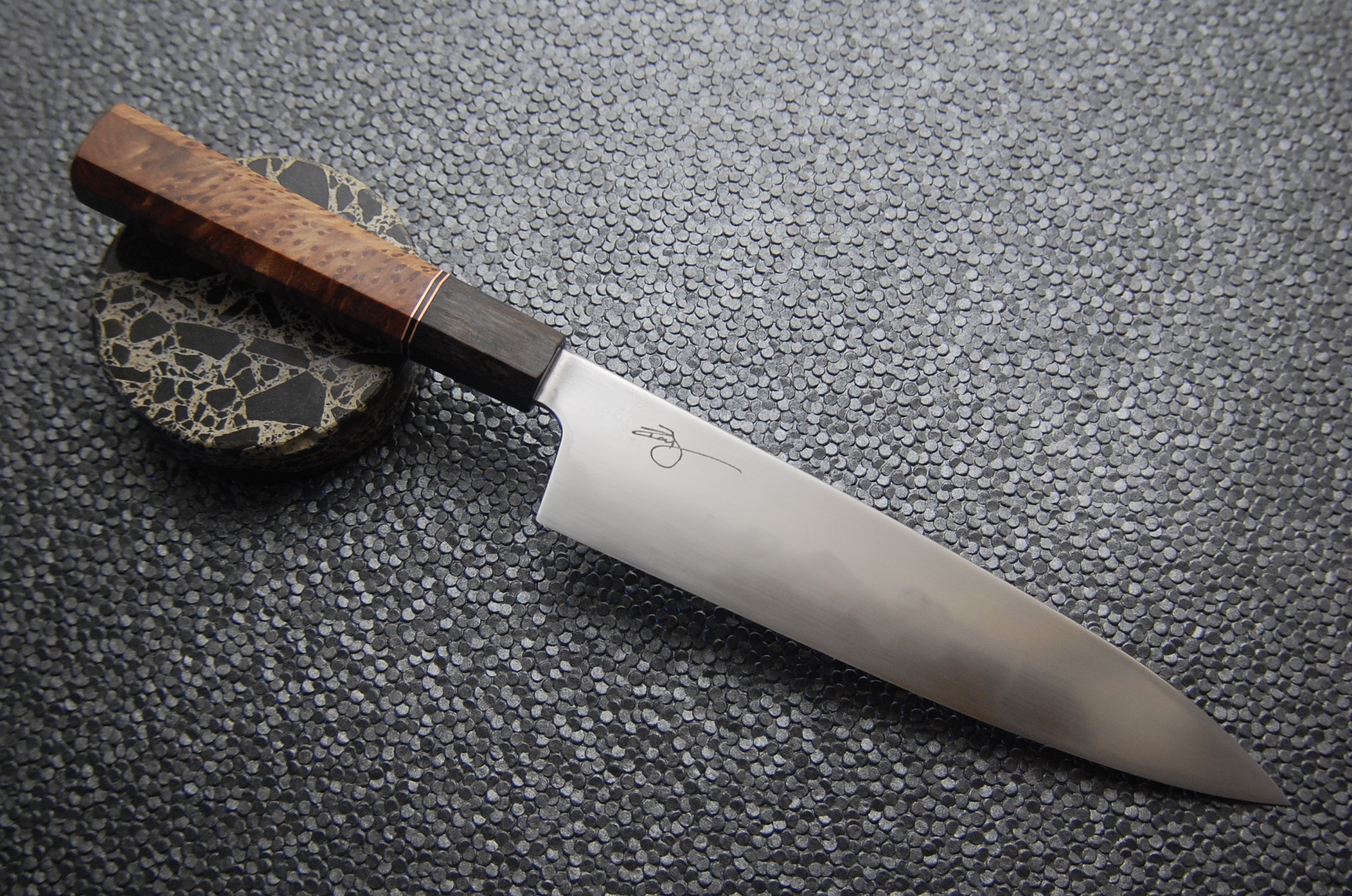The steel is 1095 high carbon and the handle consists of black lacewood, copper, G10, and redwood burl.