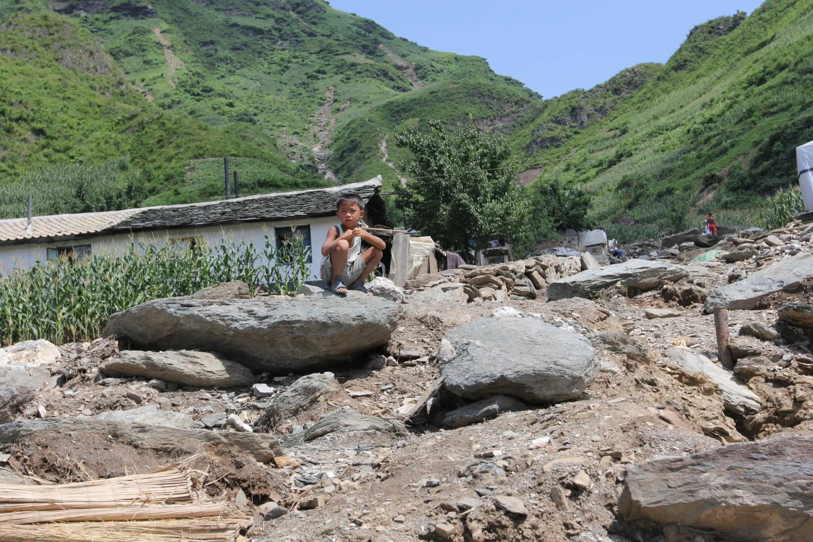 SONGCHON, North Korea _ A boy sits atop rubble left when flooding triggered a landslide that destroyed his village in Anju County, North Korea, in the summer of 2012. Photo by Jean H. Lee. All Rights Reserved.