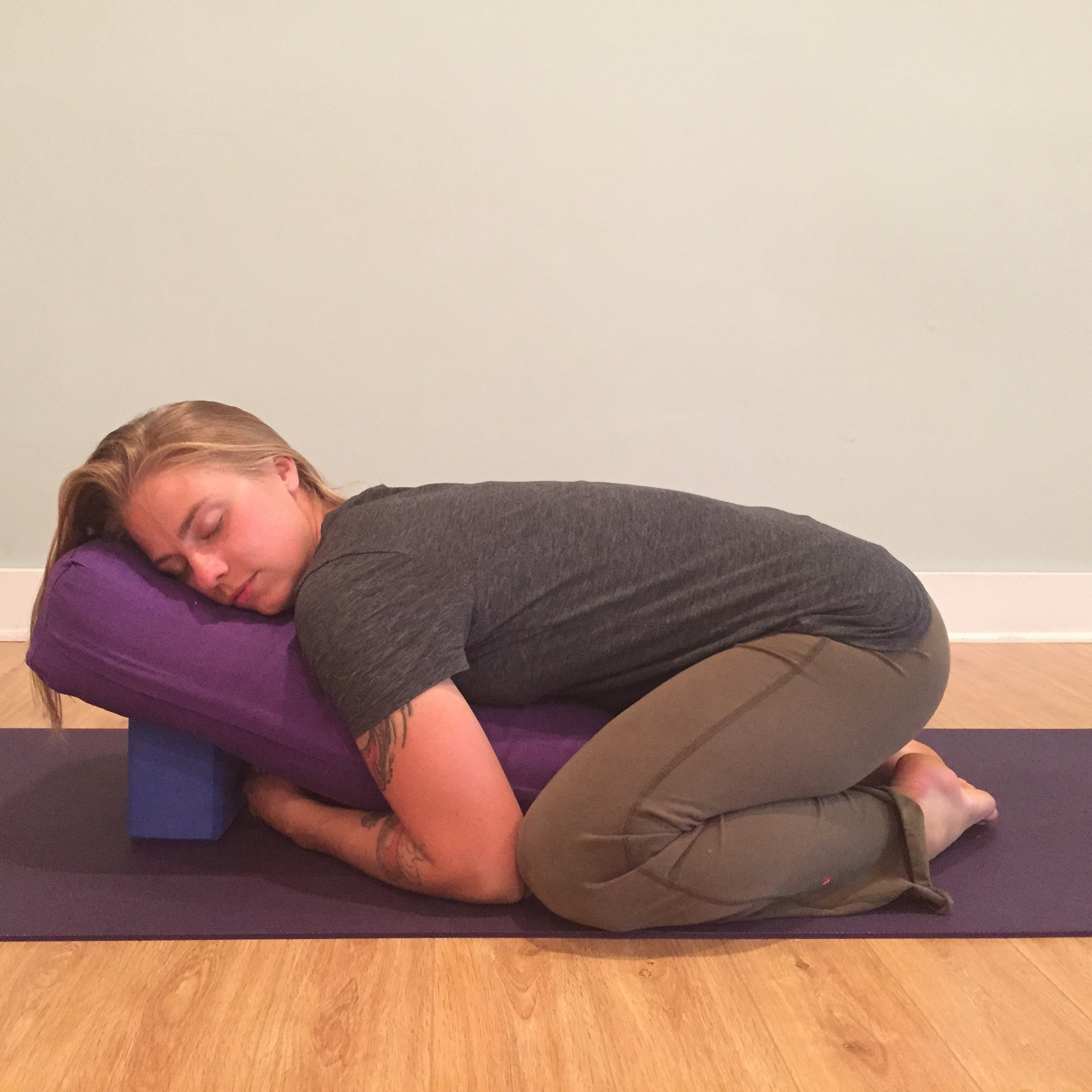 Pictured here is a supported child's pose with the support of an elevated bolster. This pose can easily be adapted at home by using pillows for support. 
