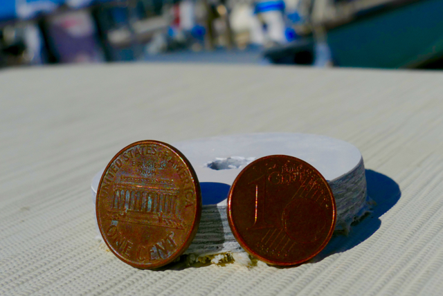 1¢ U.S. dollar and 1¢ Euro and the hull cutout. The hull is thicker at the waterline and below, and fibreglass is a hardy material, but it is still unnerving to contemplate what separates one from the great blue out there. Leica Typ 114, 10 July 2015.