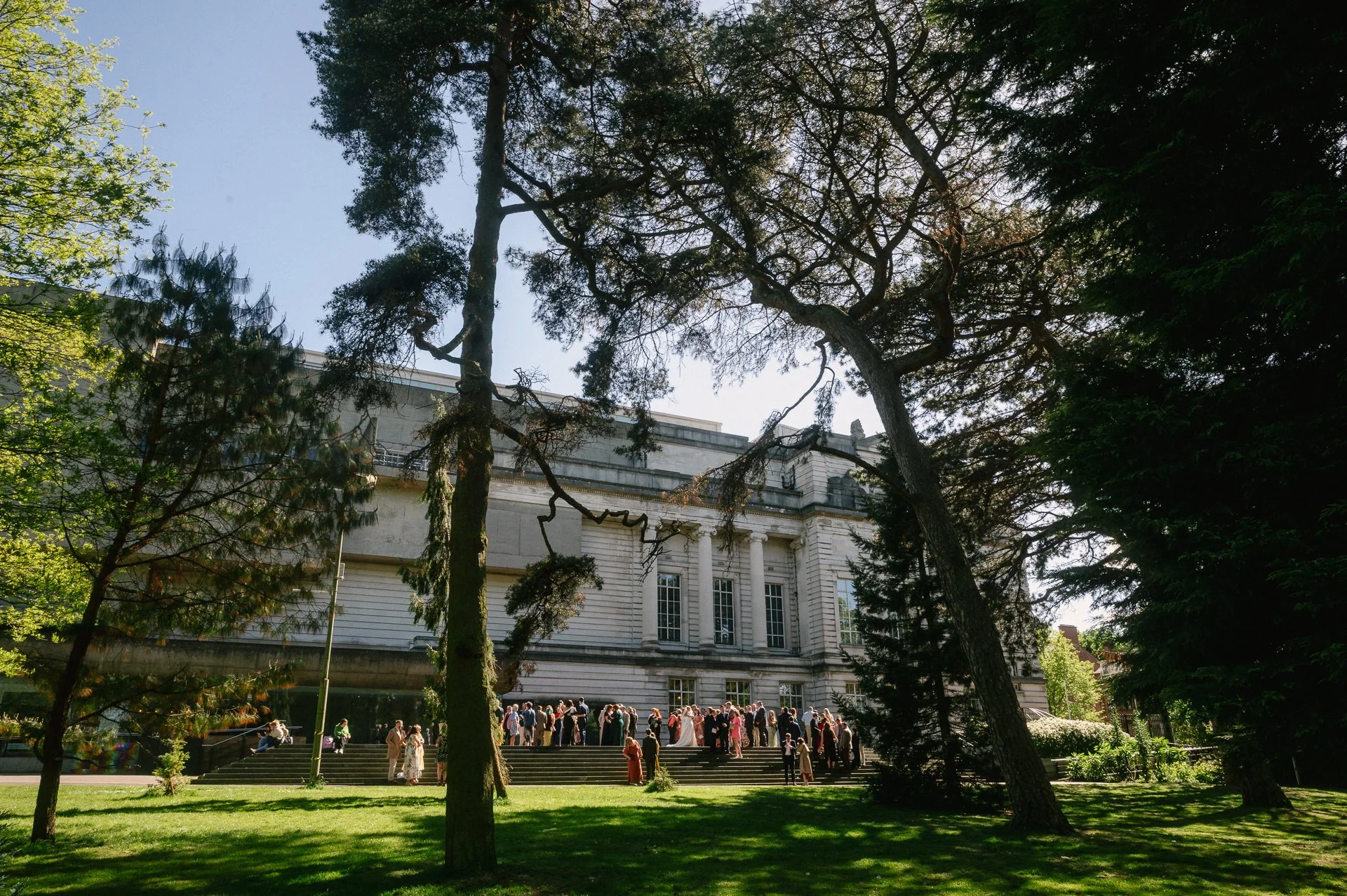 Wedding guests gathering in sunshine on front steps of the Ulster Museum