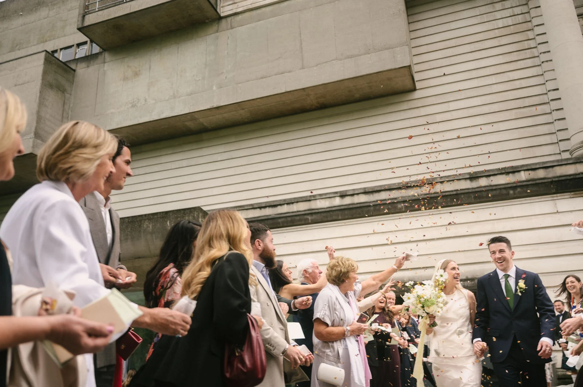 Joyful wedding photo at Ulster Museum of couple exiting the front doors in a confetti shower