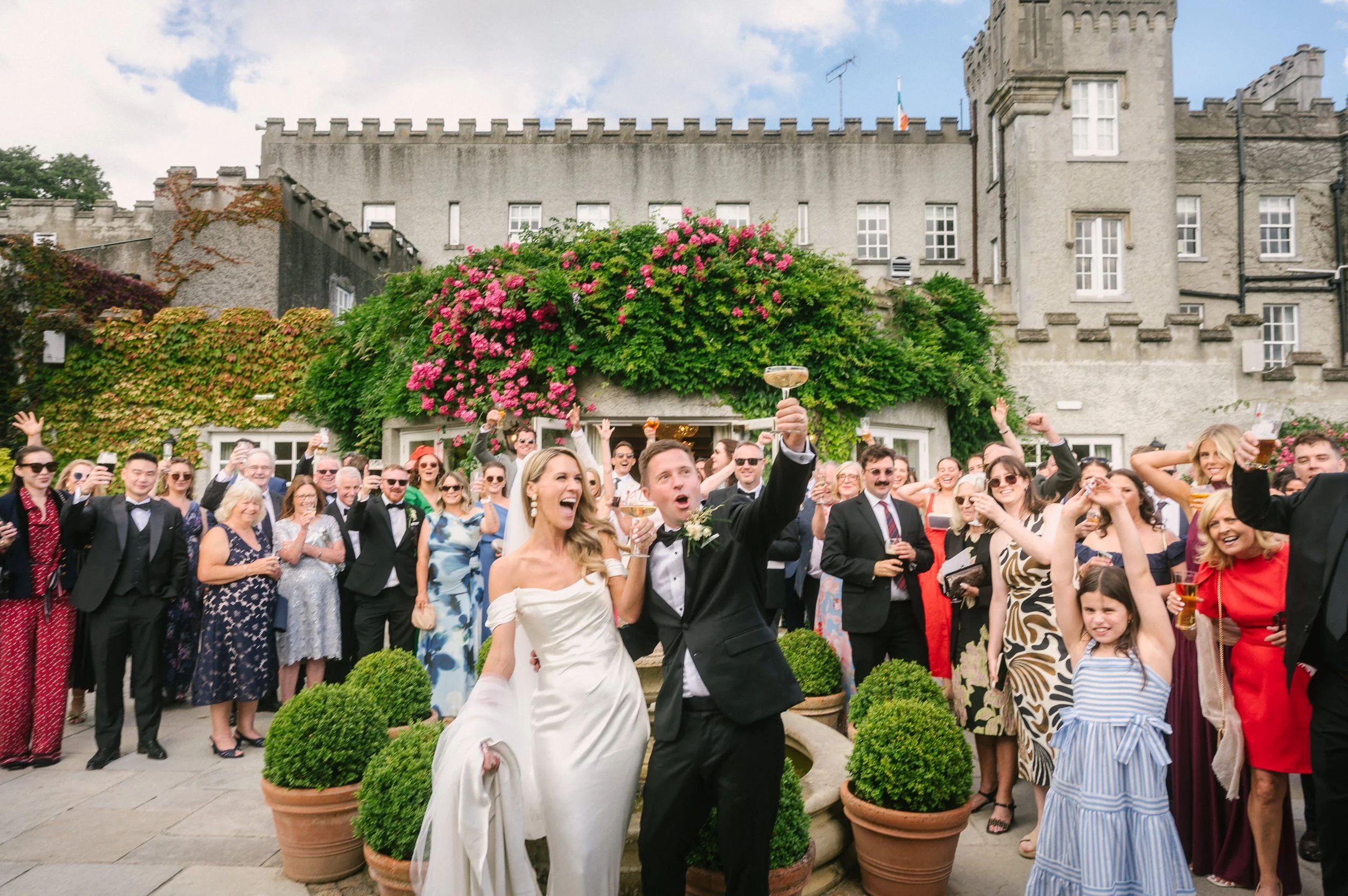 Happy wedding couple toasting champagne with guests in front of bellingham castle louth