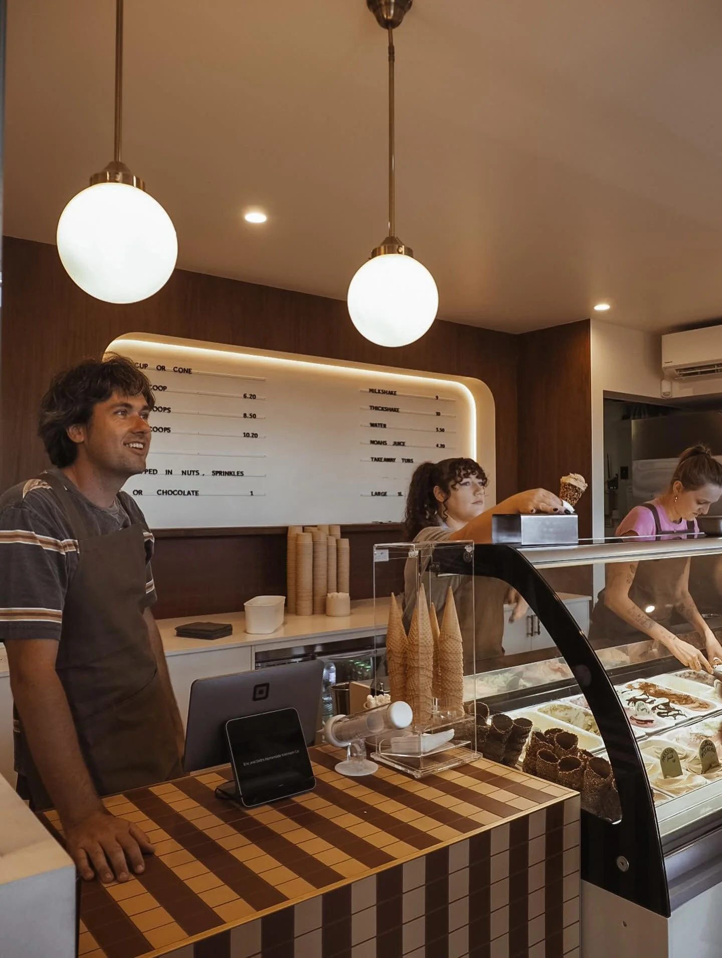 Street view of a two-story cream-colored building with a blue sign that reads 'Homemade Icecream Sorbets & Gelato'. A black car is parked in front, and a few people are visible inside through the large windows.