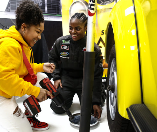   (L-R) Laya DeLeon Hayes learns to change tire from Brehanna Daniels at the Glammed-Out Auto Clinic at West Coast Customs on behalf of BUMBLEBEE, in theatres December 21 (Photo Credit: Steven Baffo)  