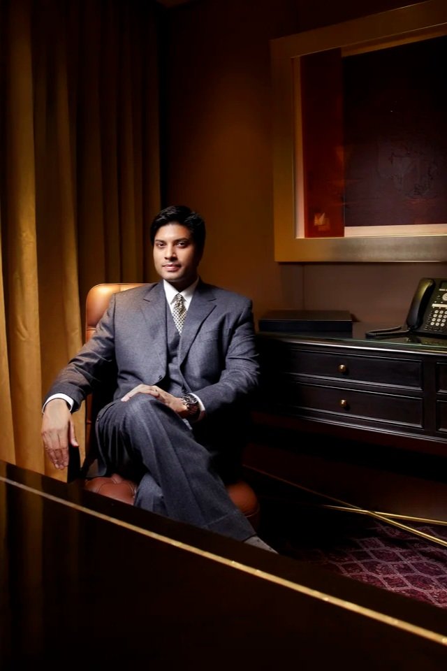 Man in business suit sitting in a luxury office, with a telephone on the desk and art on the wall.