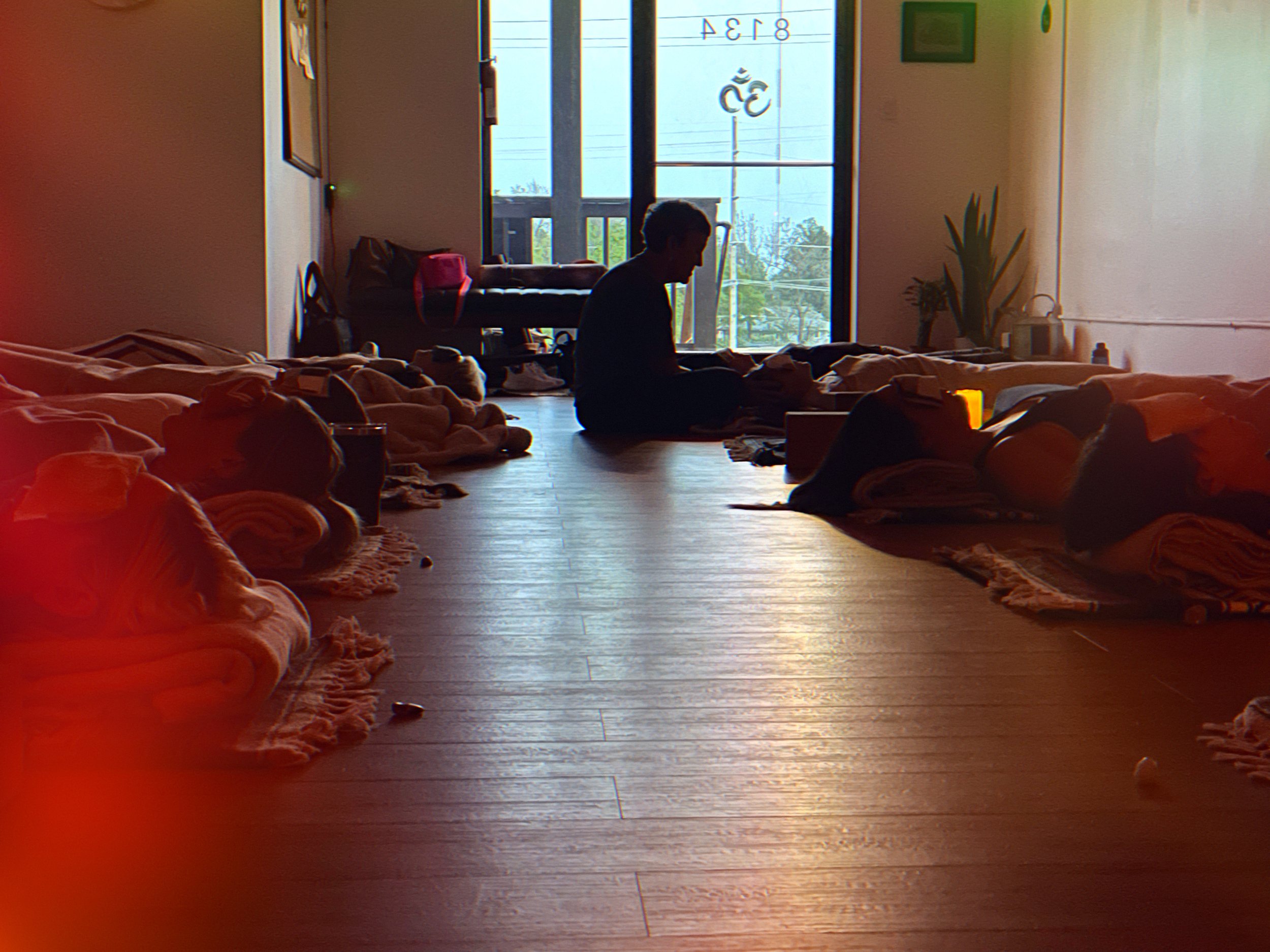 Yoga or meditation class with people lying on mats in a dimly lit room, instructor visible in the center.