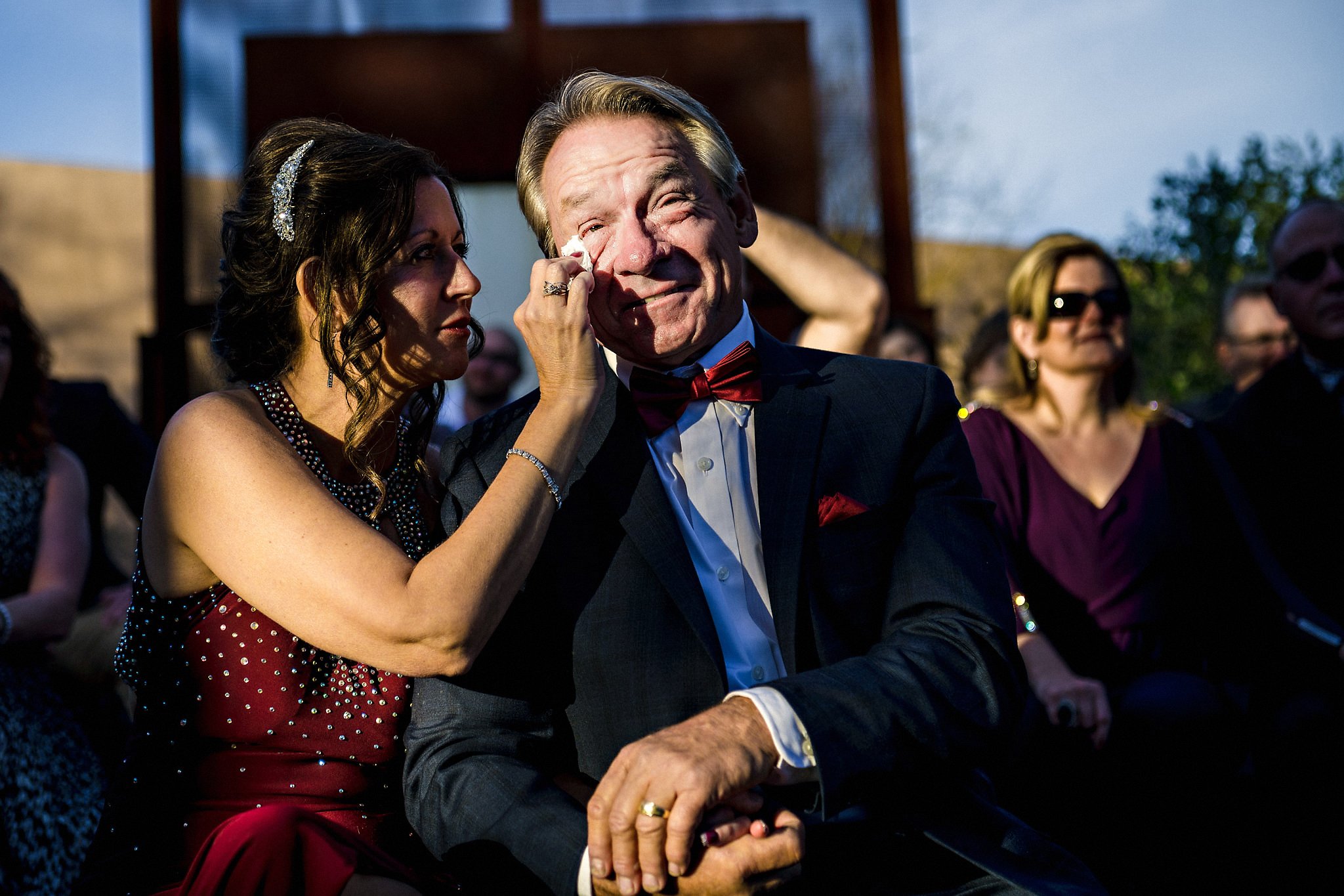 Groom's mother wiping emotional tear off of her husband's cheek during the ceremony in Desert Botanical Garden in Phoenix, Arizona