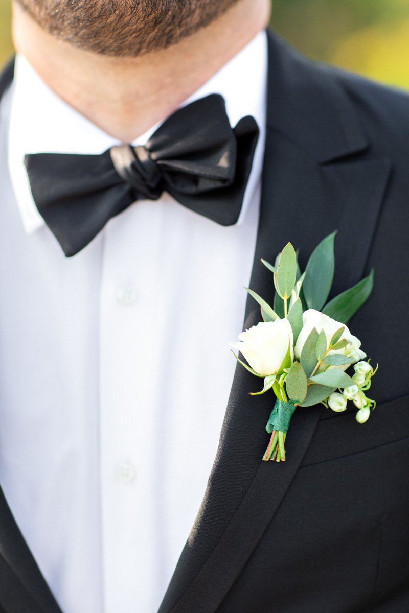 close up of groom's boutonniere of greenery, white roses, and lily of the valley
