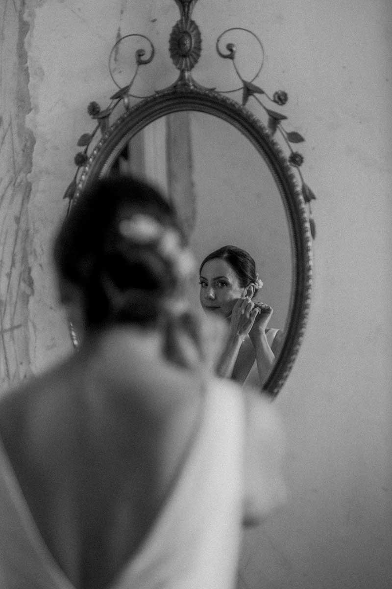  Bride putting on her earrings and looking in a mirror. 