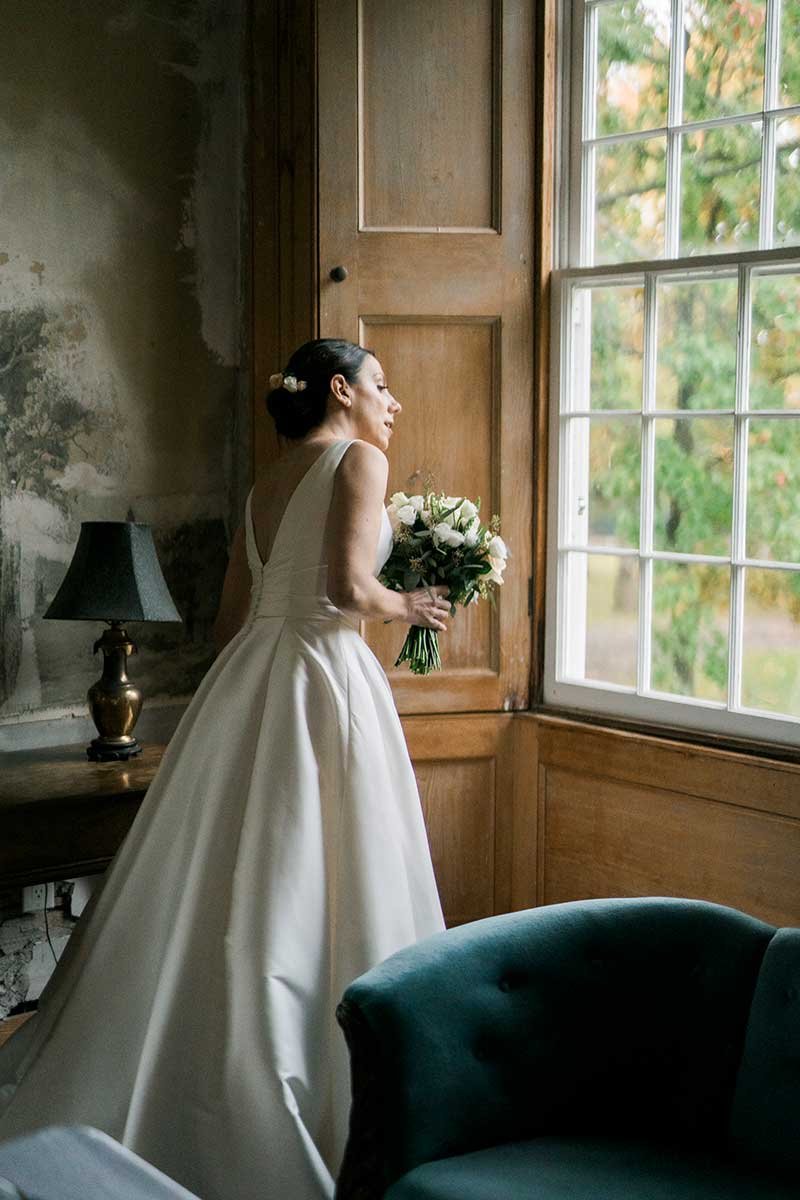  Bride holding her bouquet and peering out a window before her wedding ceremony.  