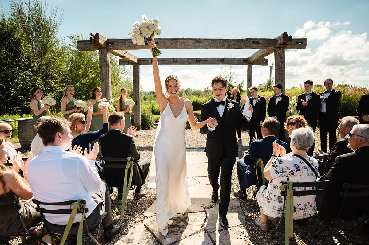 bride and groom joyfully exiting their wedding ceremony up the aisle with bride holding her bouquet overhead