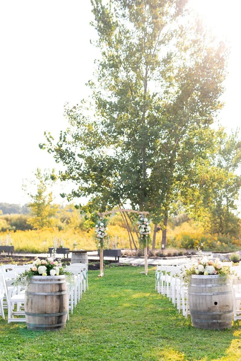 outdoor vineyard wedding ceremony with floral arbour and floral wine barrels