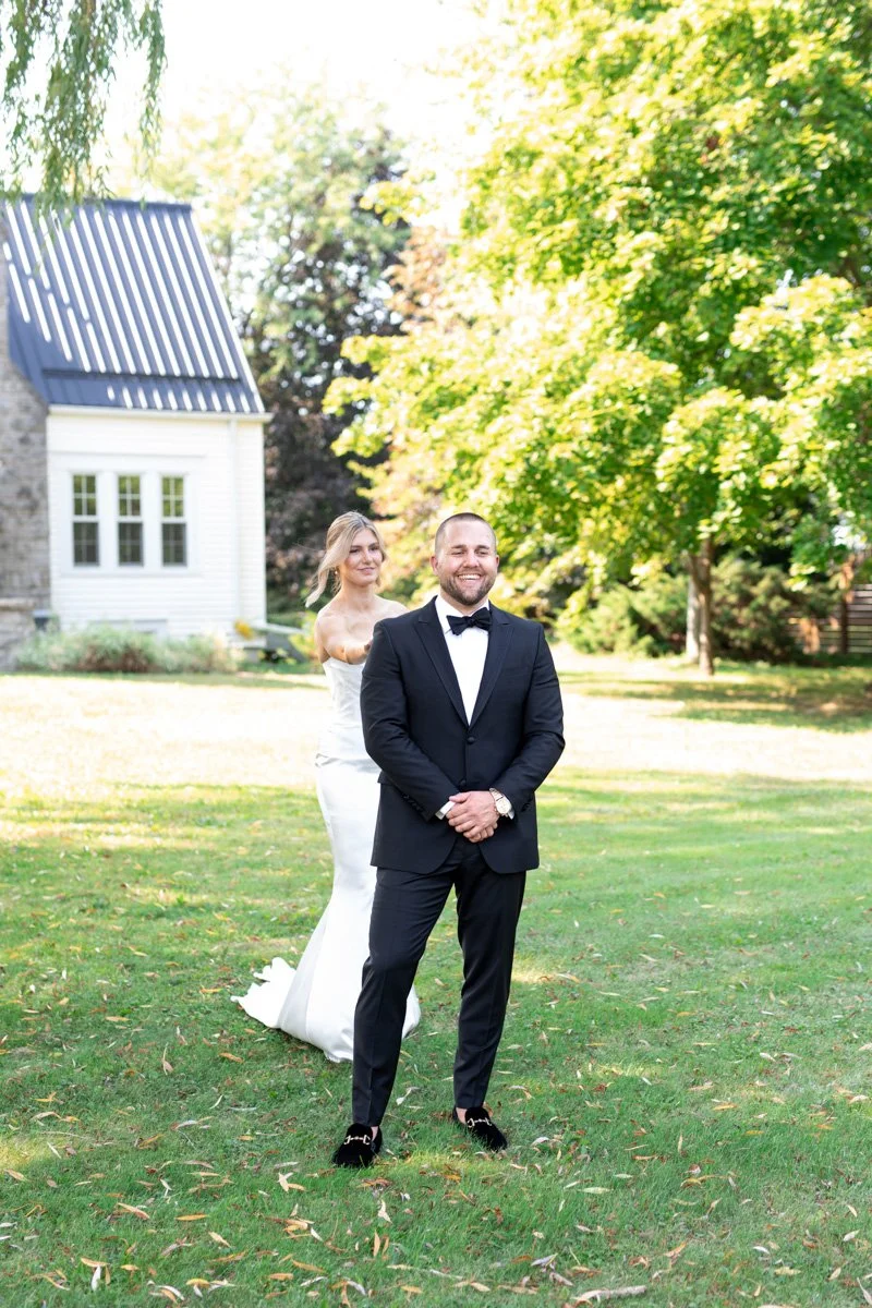 groom facing away from the bride while she walks up behind him and taps his shoulder