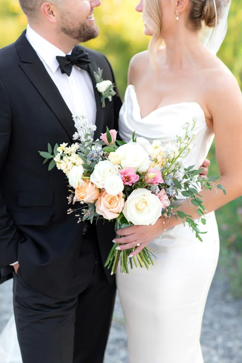 bride in a strapless gown holding a bouquet of flowers and groom wearing a black suit and bowtie from the shoulders down looking at each other