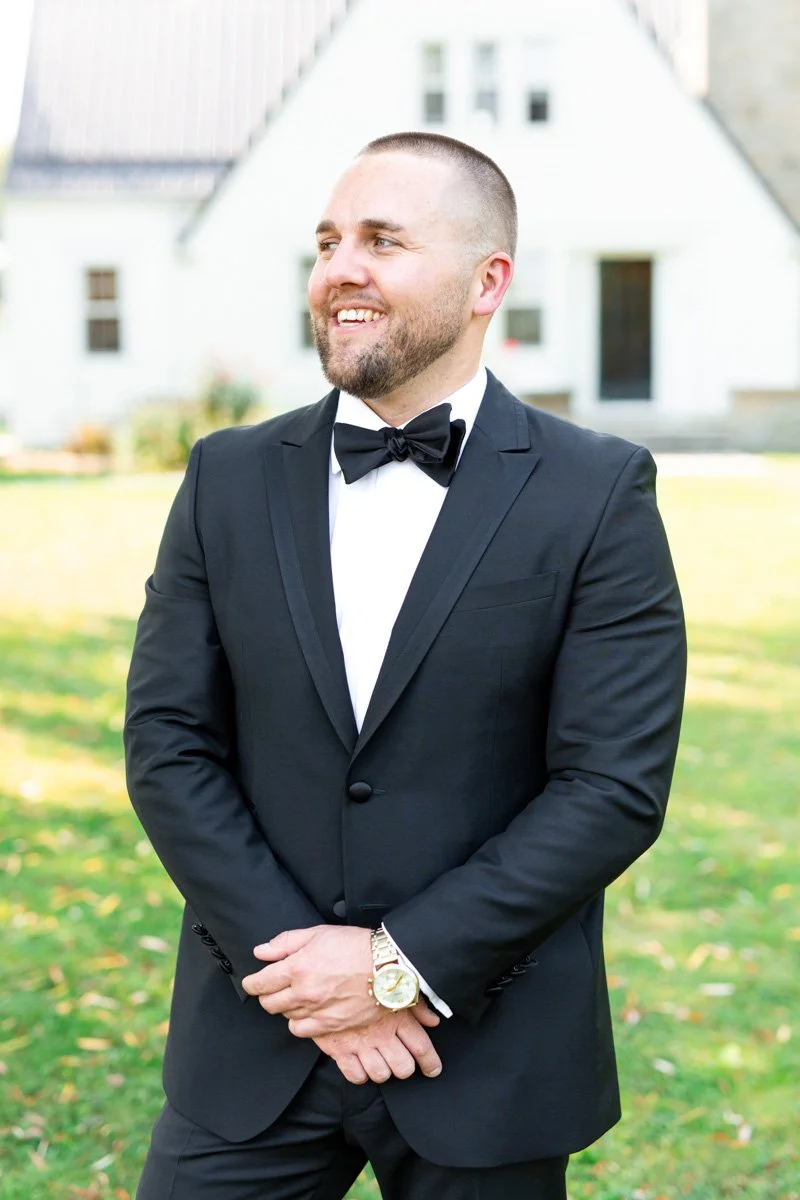 groom wearing a black suit and black bowtie standing outside and smiling