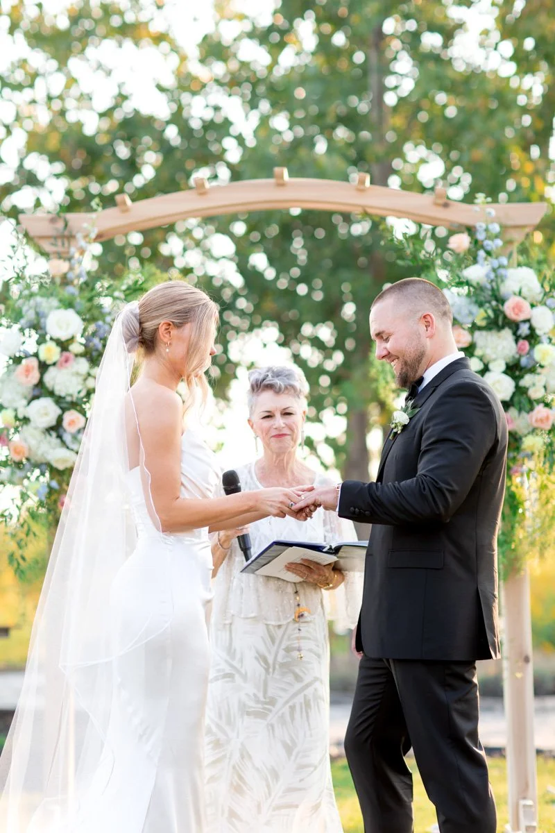 bride putting ring on groom's finger during their outdoor wedding ceremony
