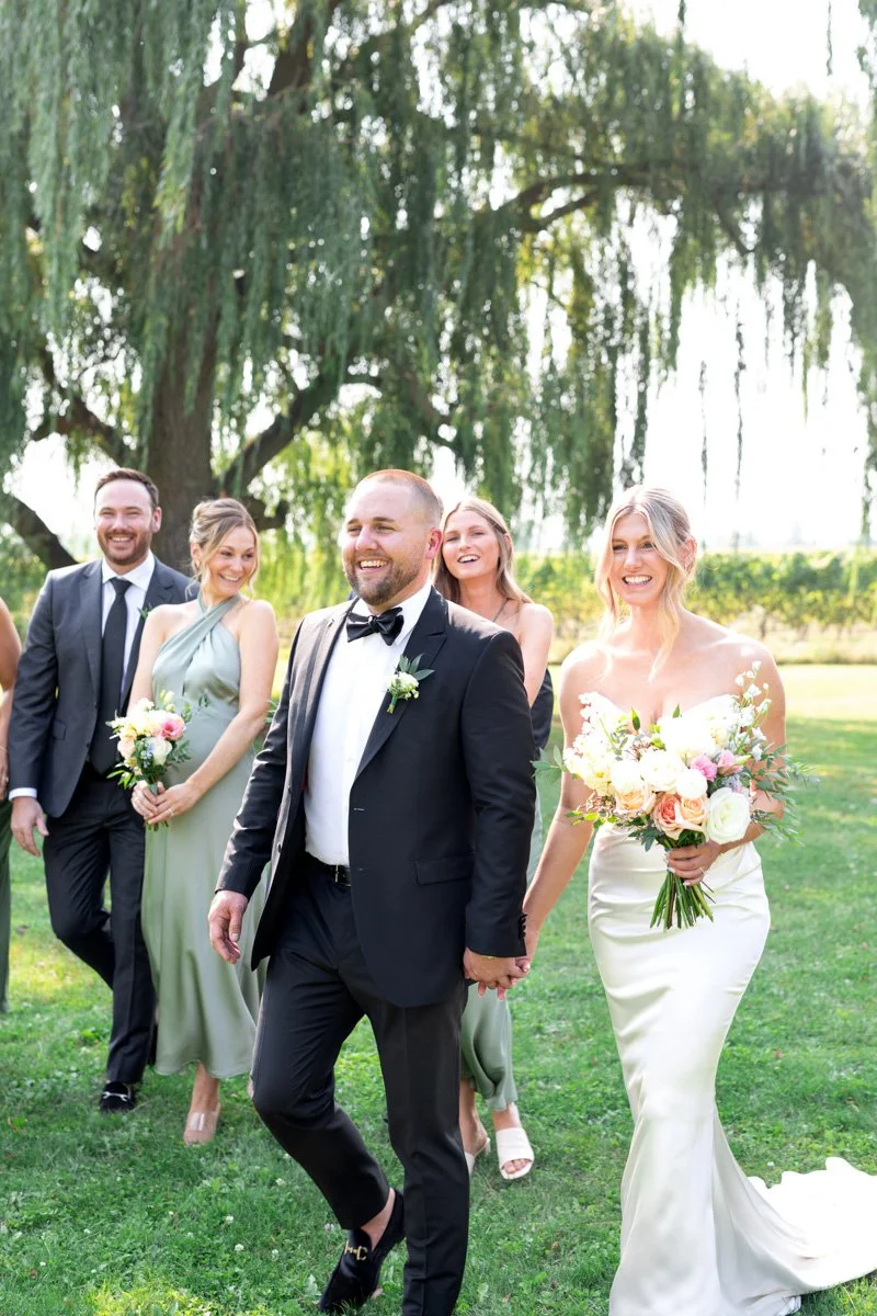 wedding party laughing and walking together with a vineyard and willow tree background
